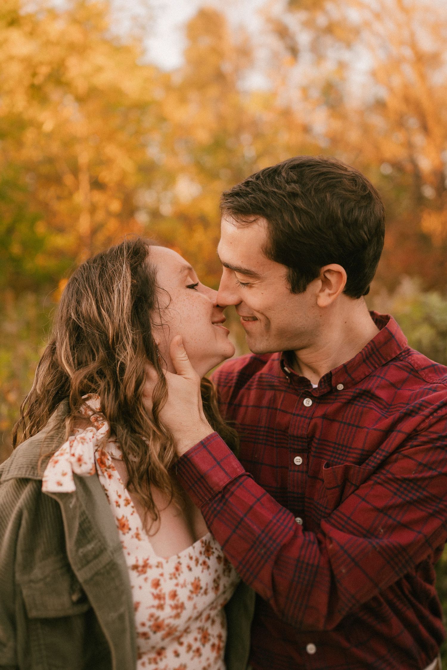 A romantic couple shares a tender moment in a park during golden fall season.