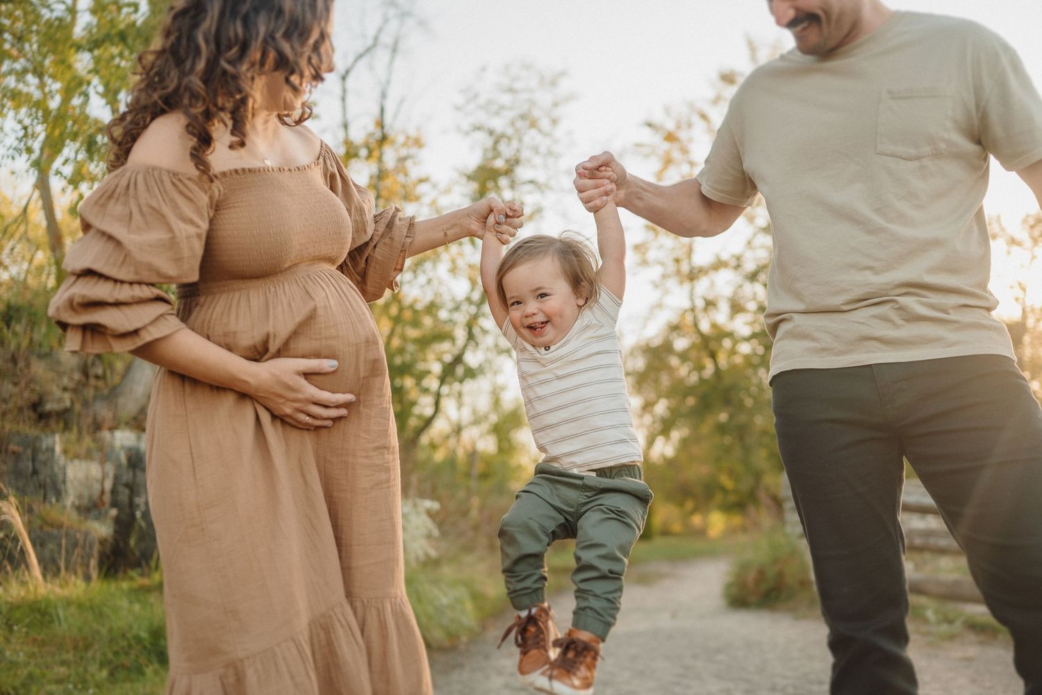 A young child joyfully swings between two adults on an outdoor path during golden hour.