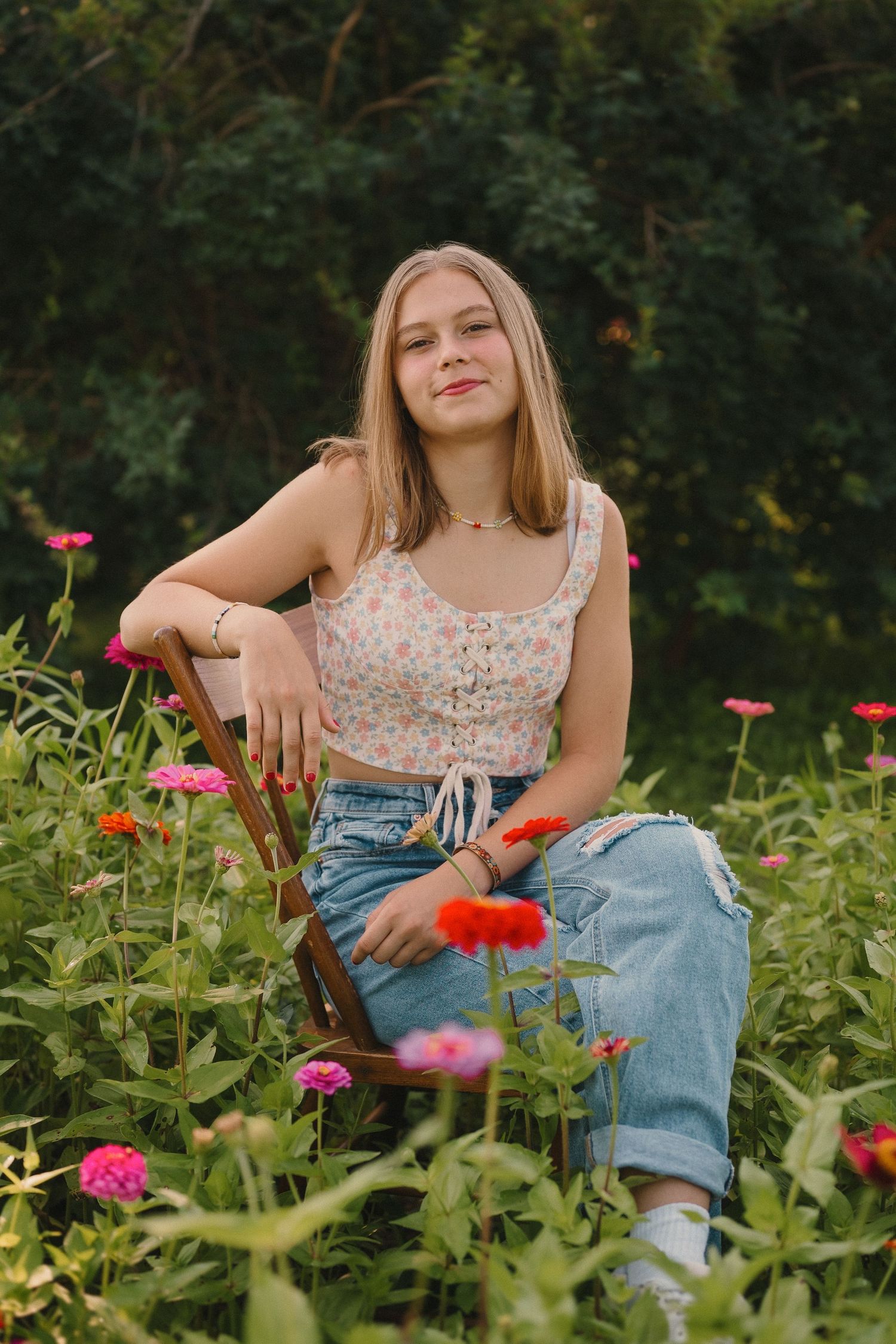 A relaxed summer portrait in a garden with vibrant red zinnias, featuring casual denim and a floral top.