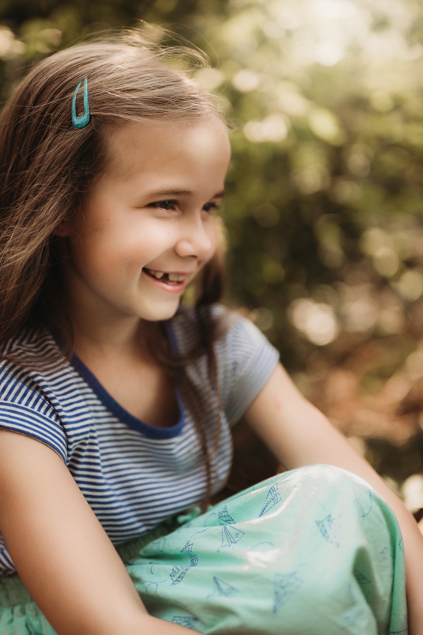 A close-up portrait shows someone smiling while wearing a striped shirt and turquoise hair clip.
