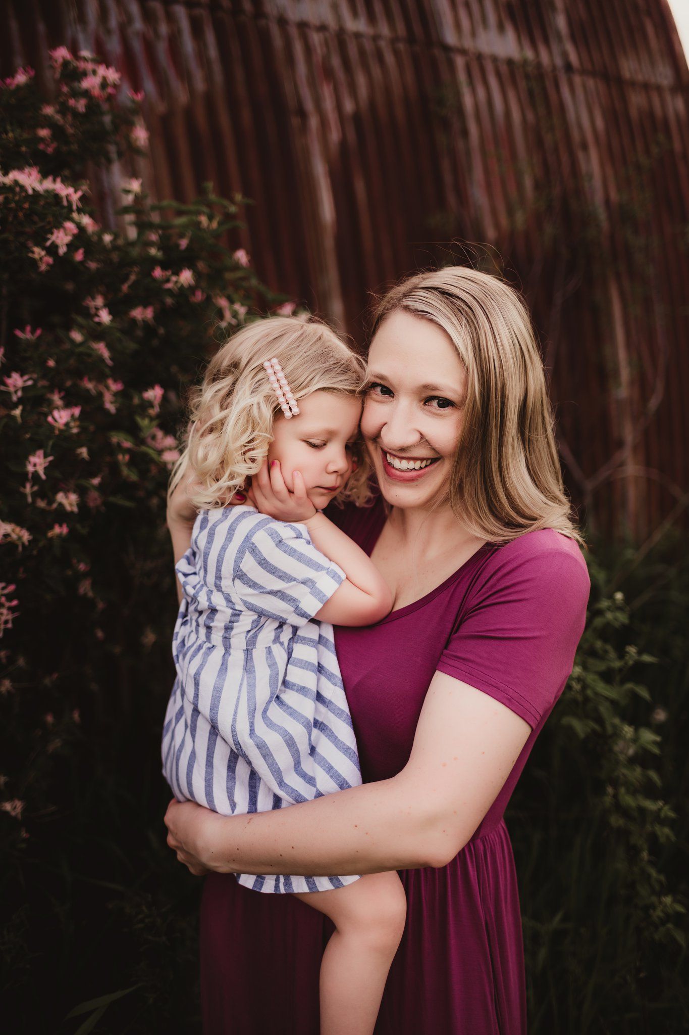 Intimate portrait against rustic barn backdrop with burgundy dress and striped outfit.