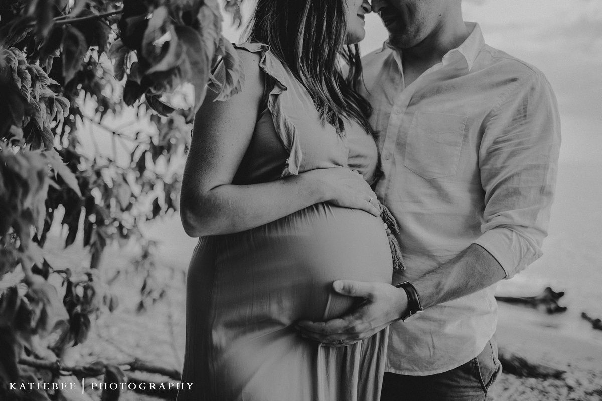 Black and white maternity photo of couple embracing outdoors with focus on the pregnant belly.