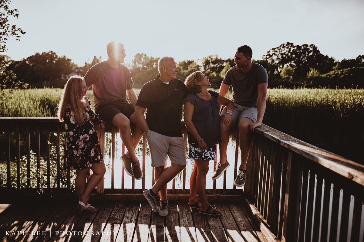 Family group posed together on wooden deck during sunset photoshoot.