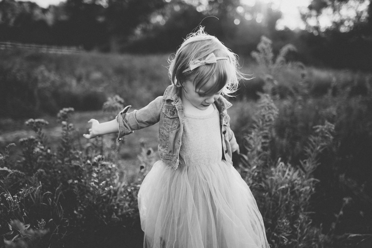 Black and white portrait of a small child in a tulle dress twirling in a meadow at sunset.