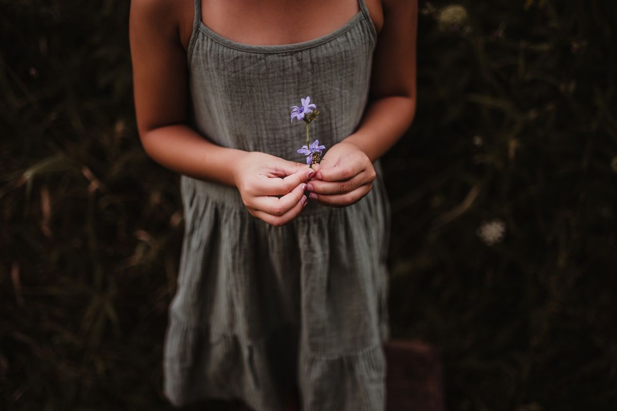 Closeup of hands holding a delicate purple wildflower against a gray dress.