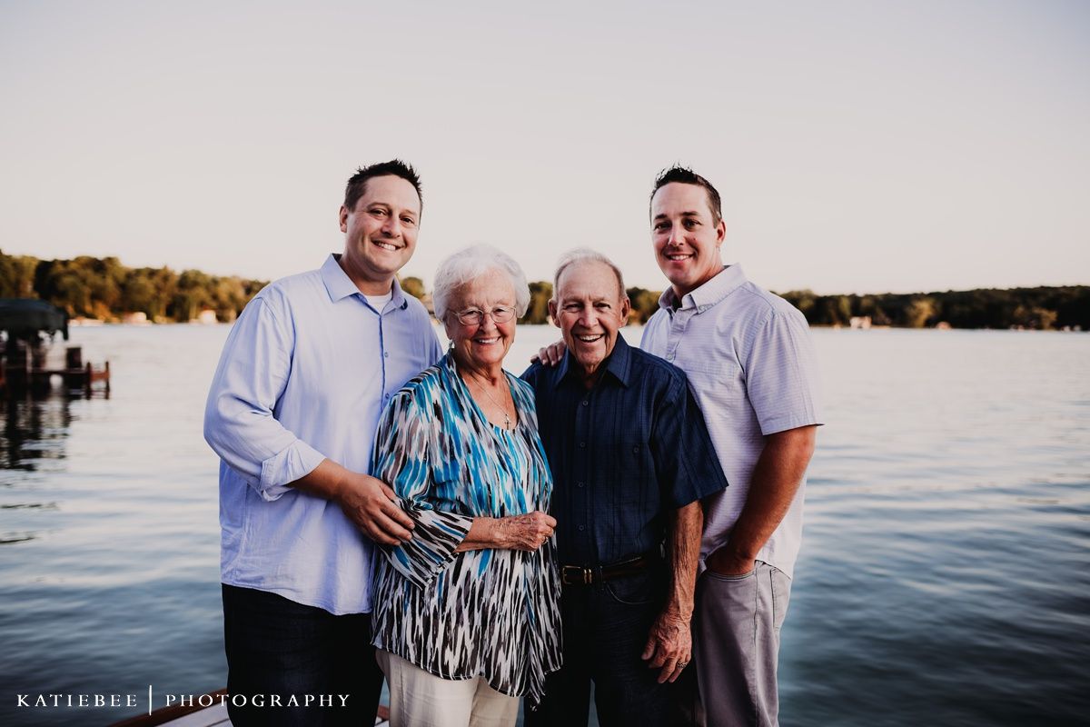 Sunset family portrait of small group standing together by lake with fall colors in background.