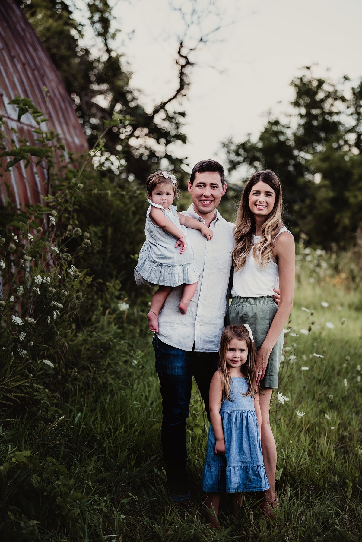 A family portrait against a rustic barn backdrop in soft evening light.