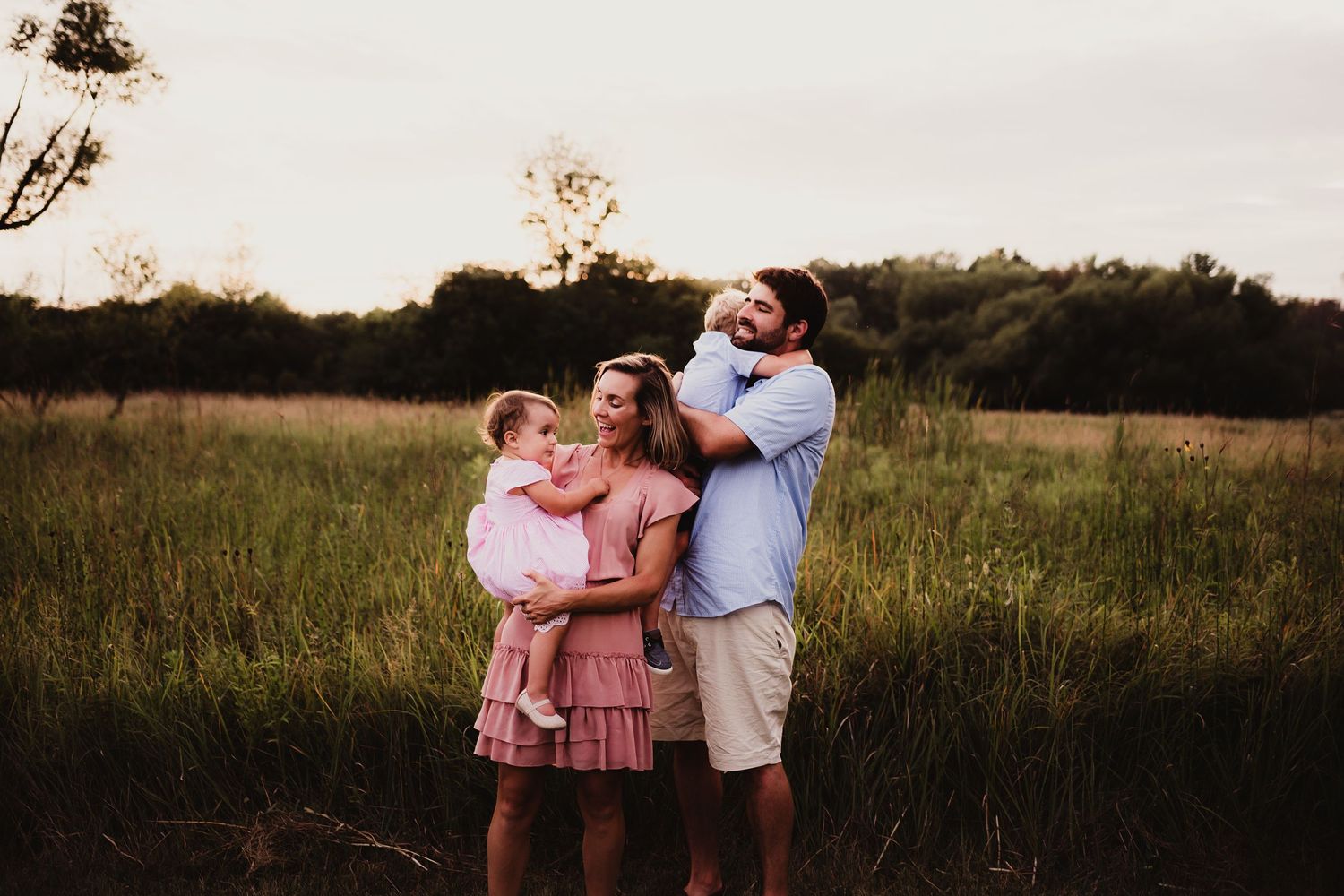 A family embraces while standing together in a golden field at sunset.