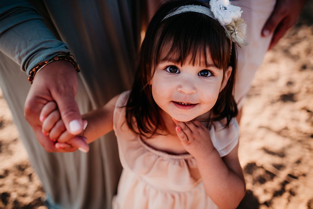 Small child wearing a light pink dress with a white hair accessory smiles at the camera.