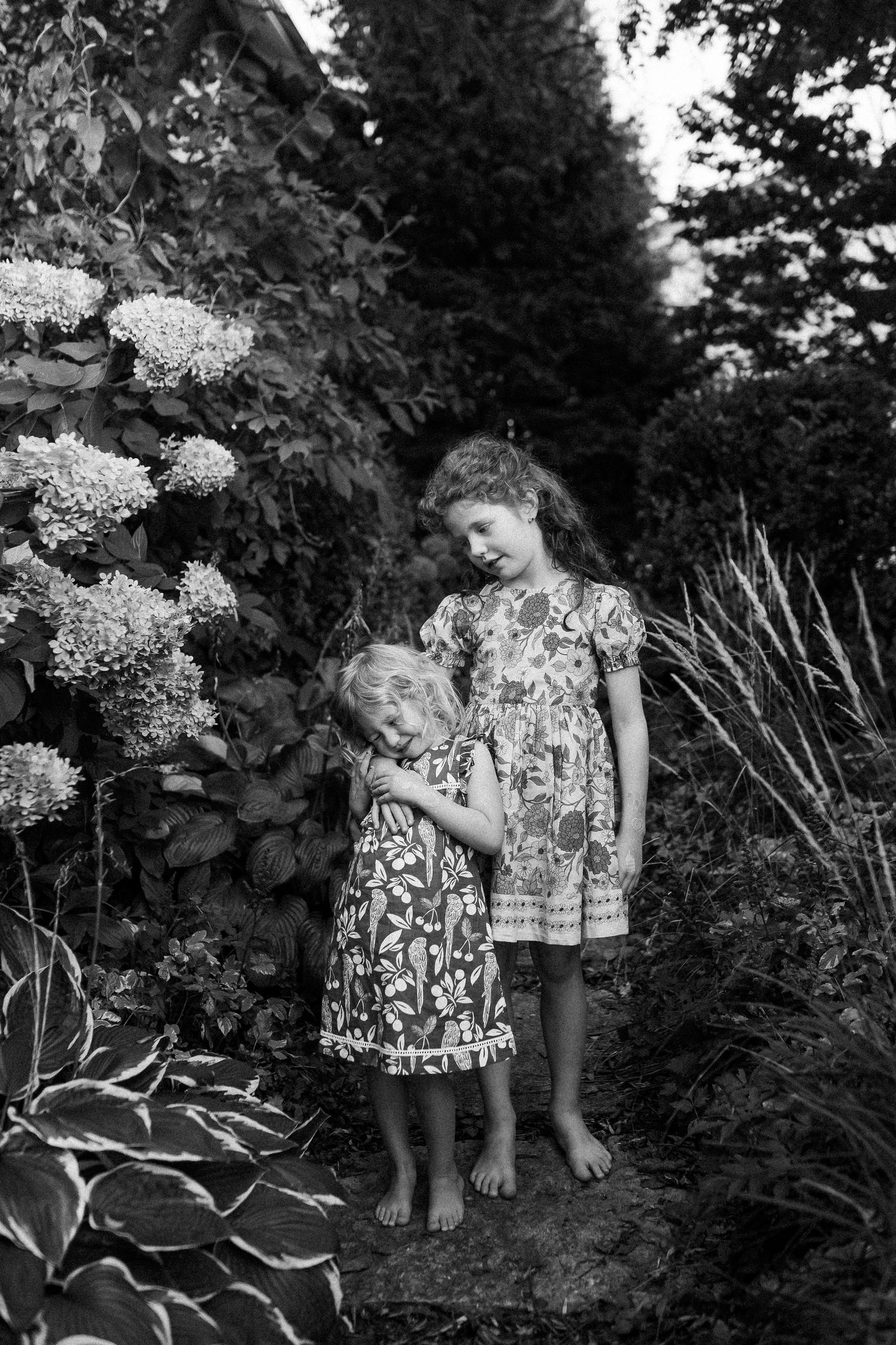 Children exploring among white hydrangea flowers in a lush garden setting.
