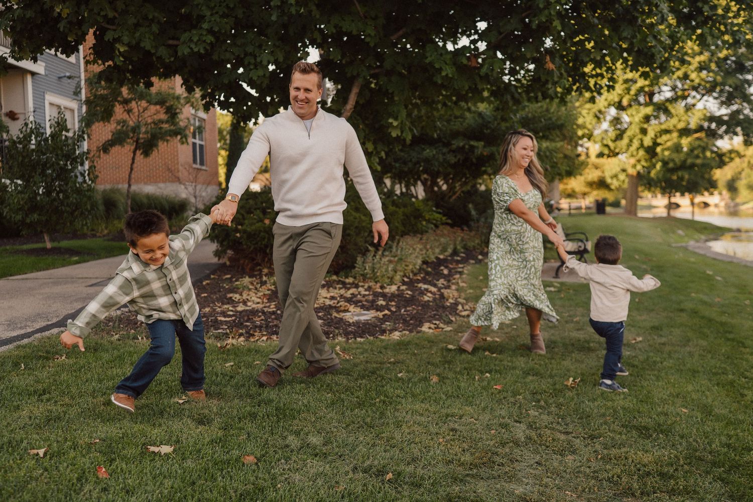 Family playing and dancing together on a grassy lawn during golden hour.