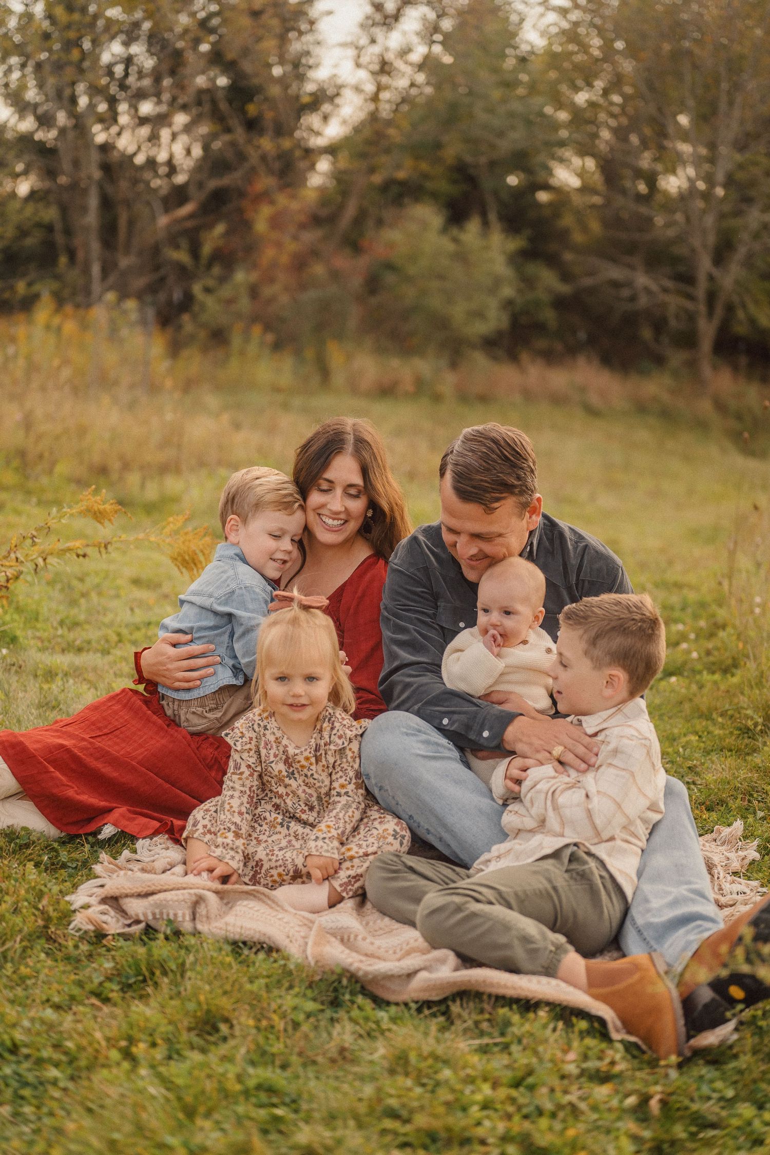 A family sits together on a blanket in a golden field during fall.