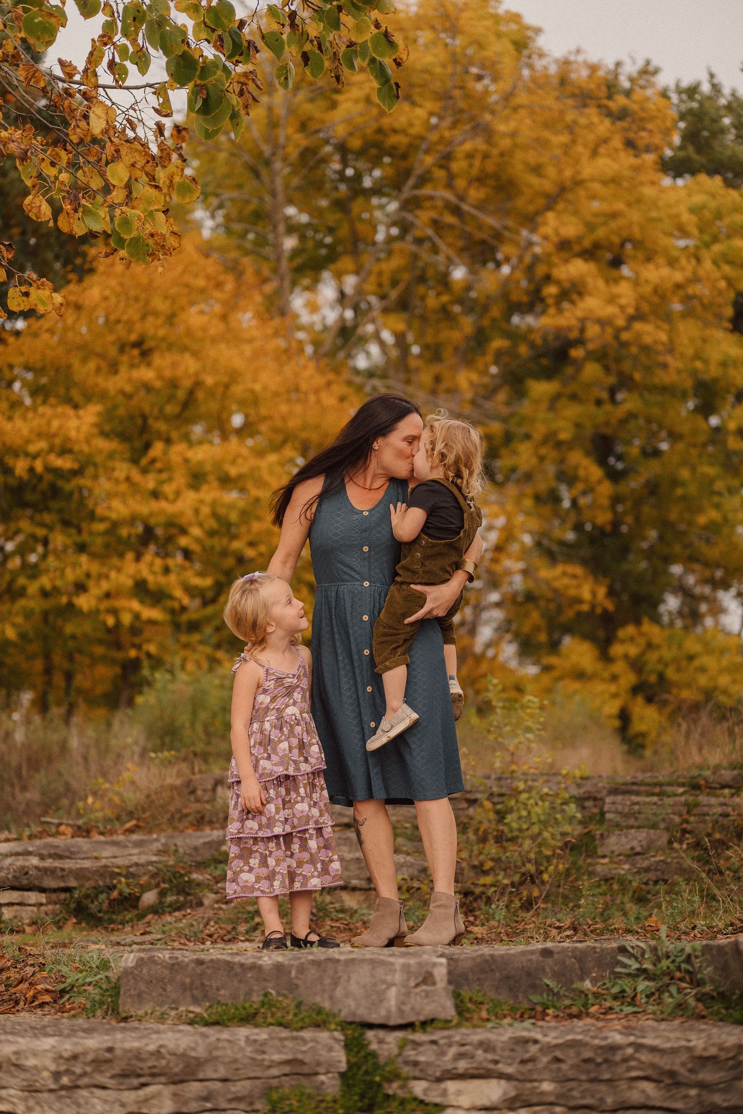 A tender autumn moment captured on stone steps surrounded by golden foliage in a natural outdoor setting.