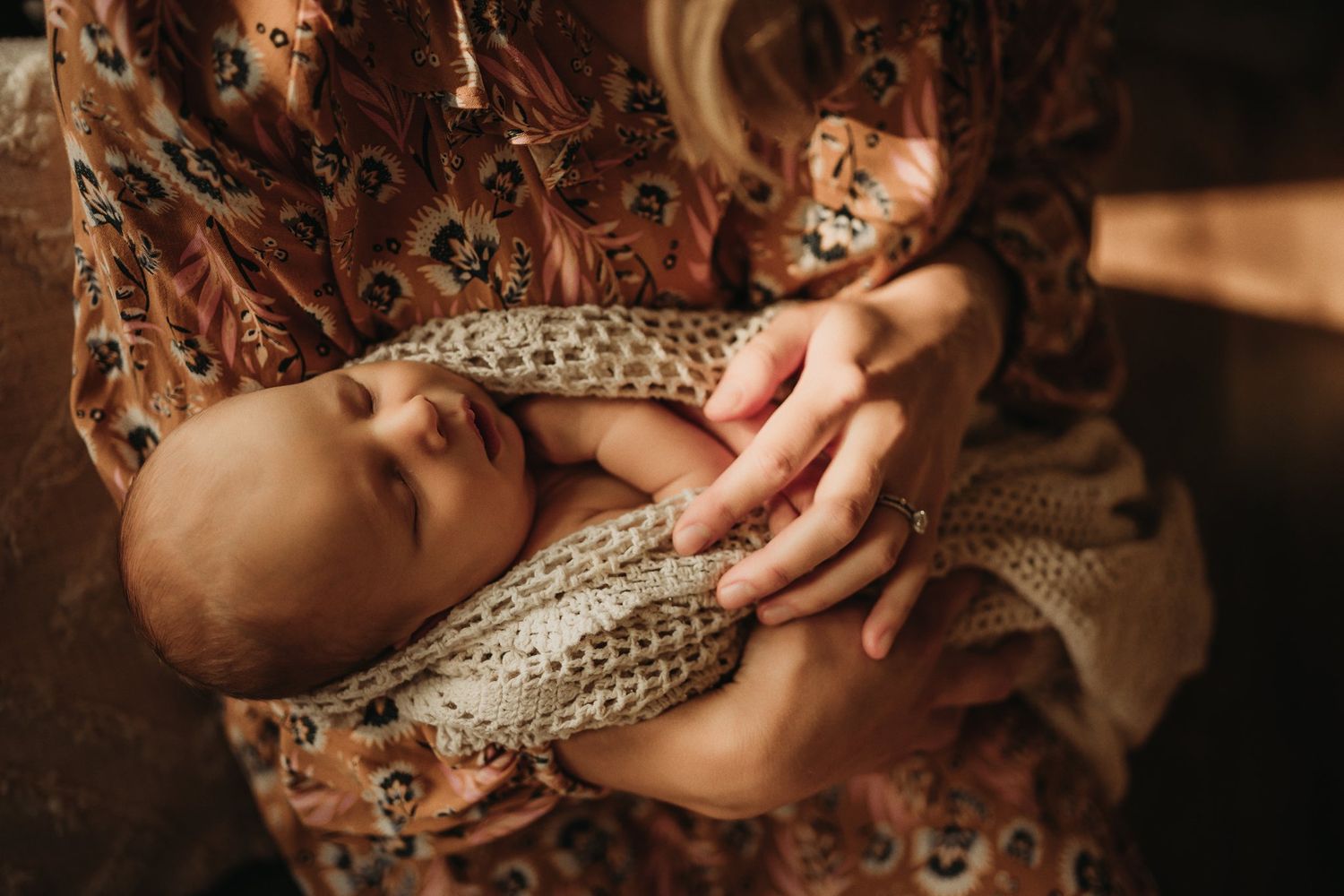 Close-up of newborn sleeping peacefully in knit blanket on mother's lap.