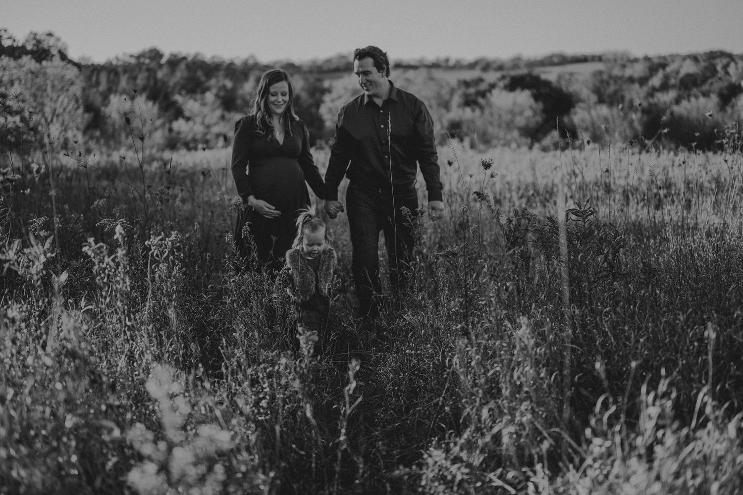 Black and white photo of couple walking through a wildflower field.