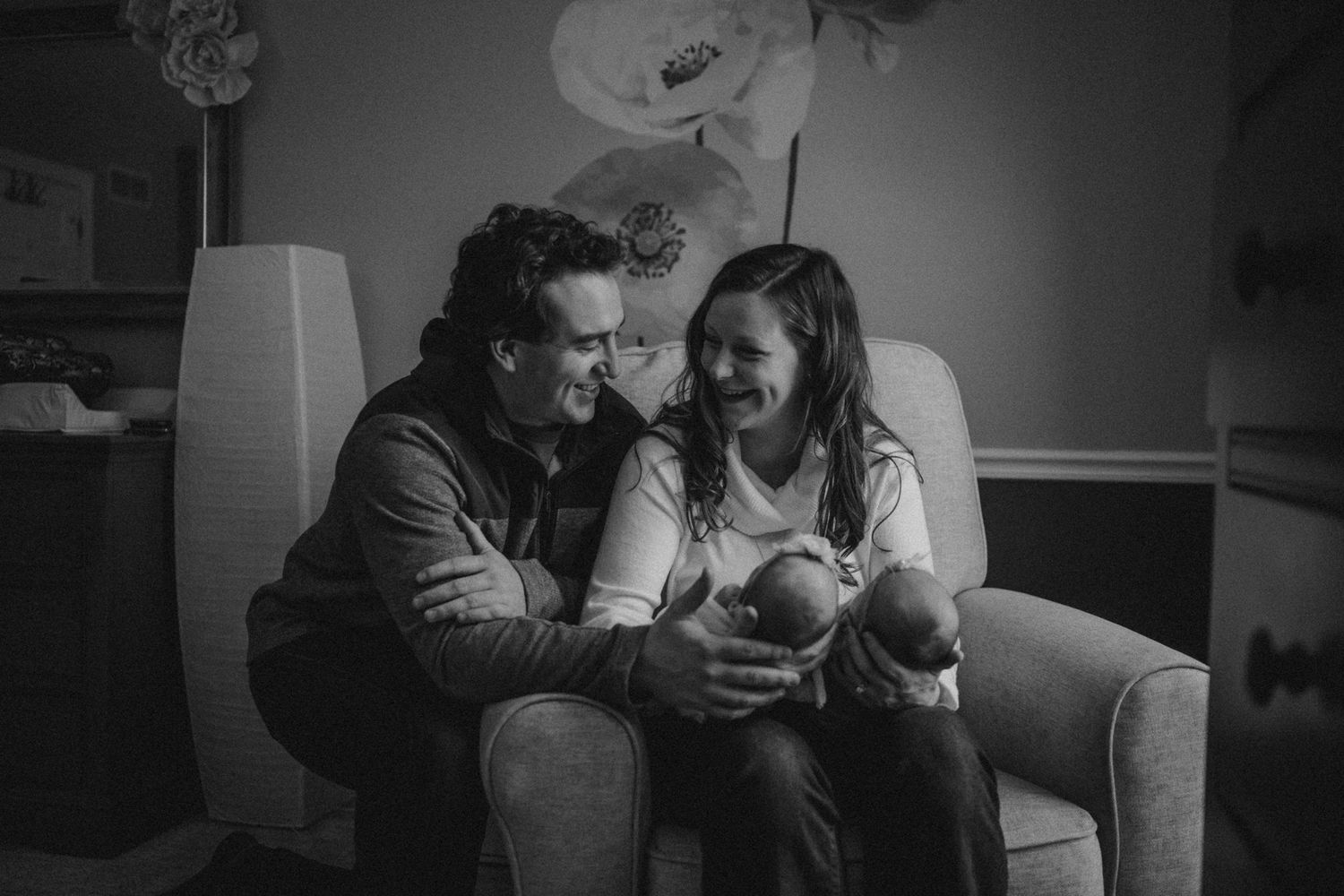 Black and white portrait of family moment with newborn twins on living room couch.