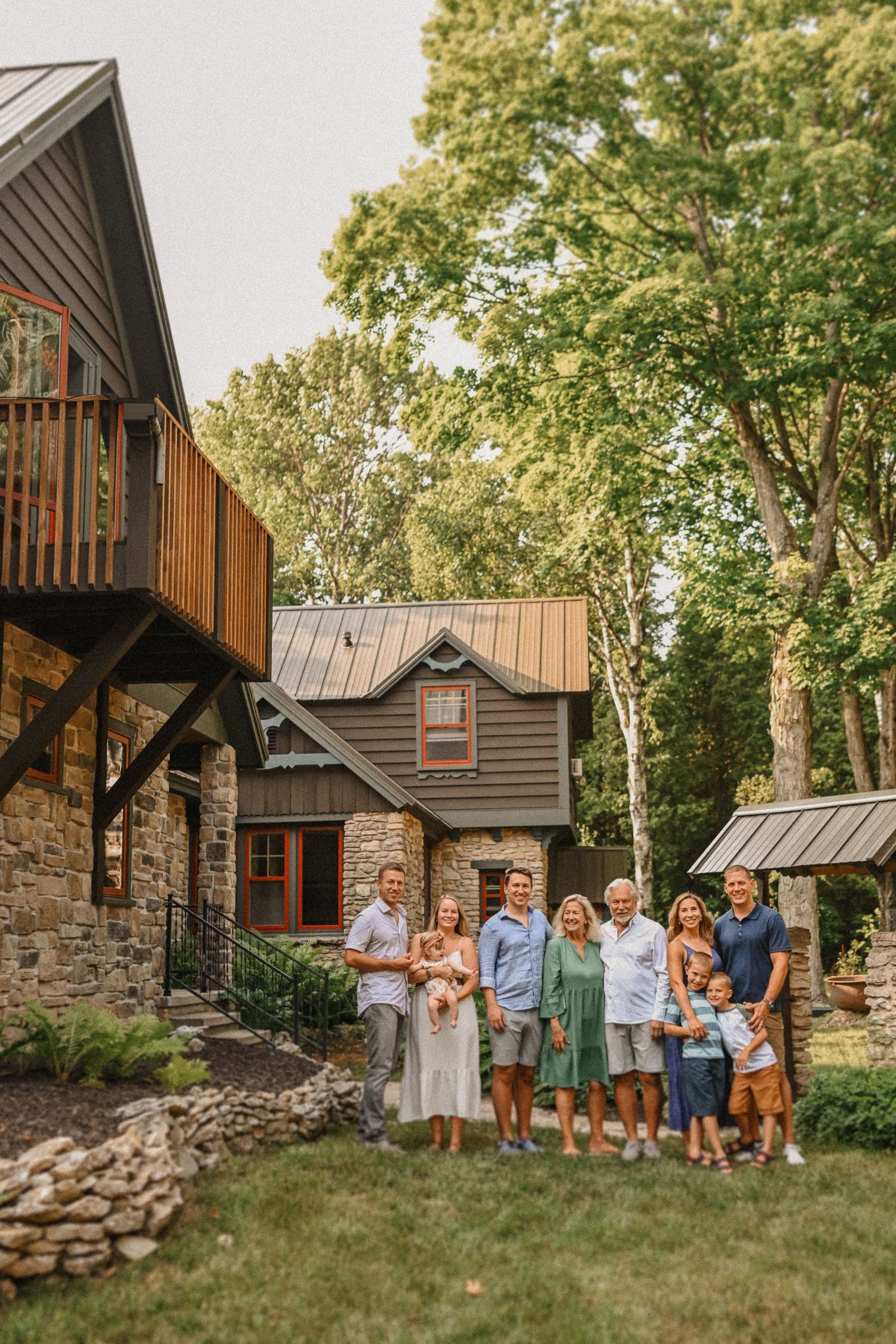 A family gathering outside a charming stone and wood cottage with natural landscaping.
