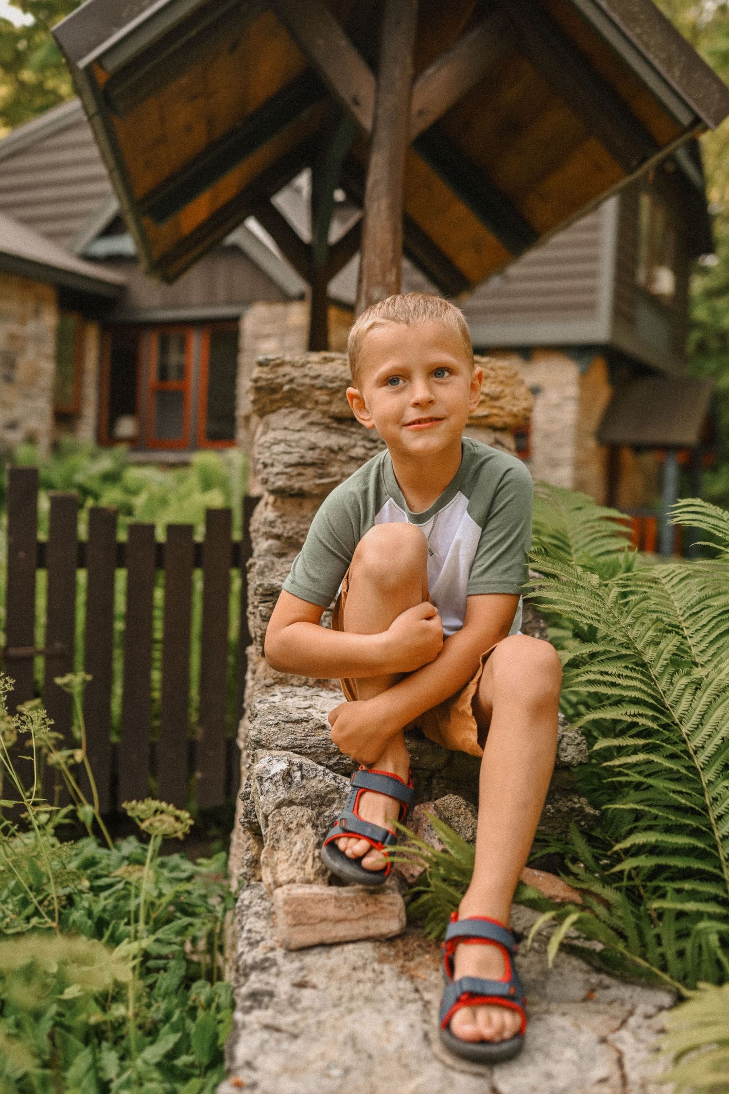 Summer portrait by a stone wall with ferns and rustic cottage architecture in background.