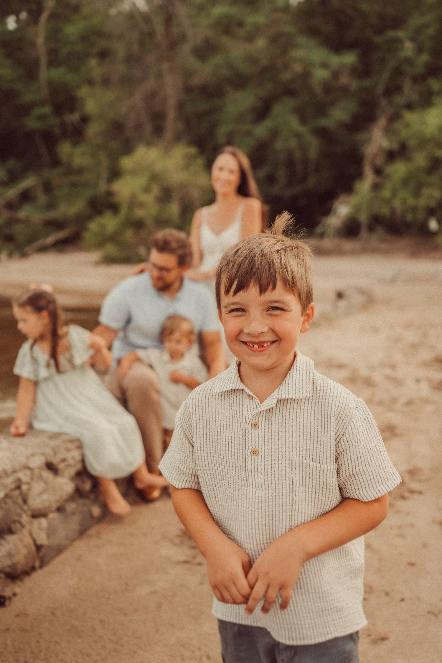 A candid beach family photo with everyone sitting on rocks by the shoreline.