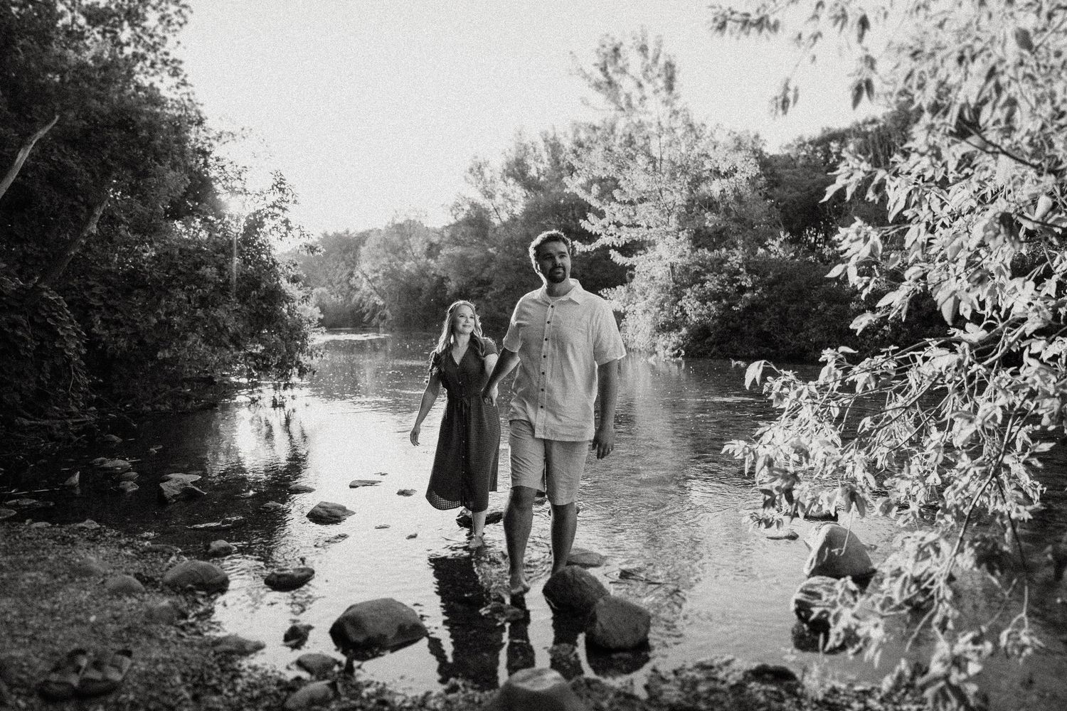 Black and white photo of two people standing on rocks in a river surrounded by trees.