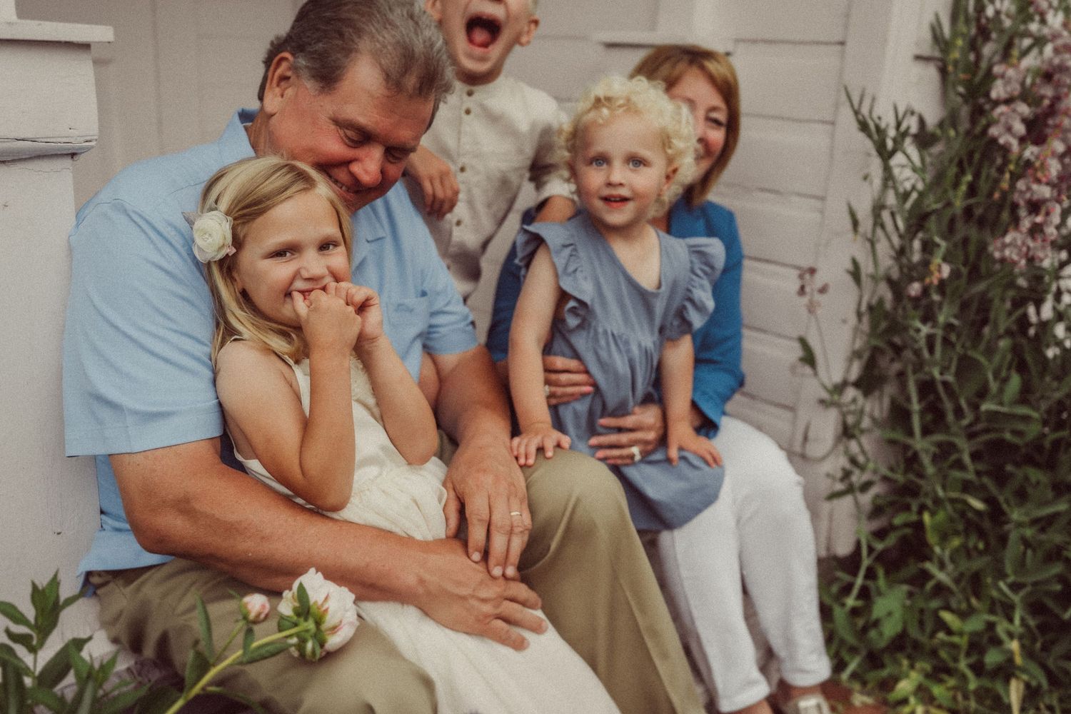 Family sharing loving moment together on white farmhouse porch with flowering garden.