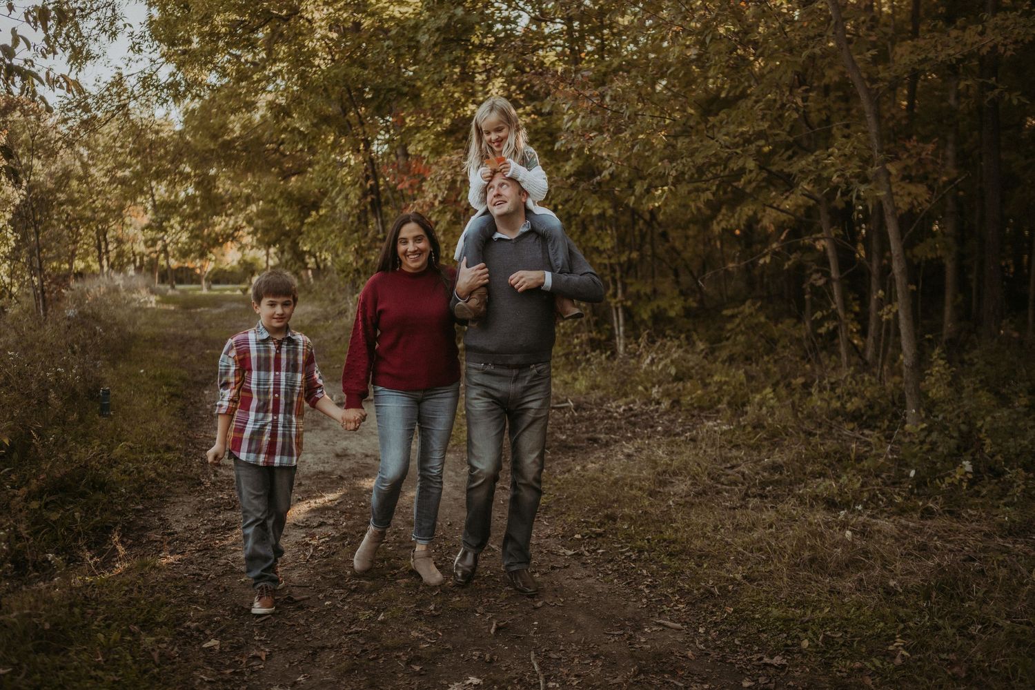 Family walking together on forest path during golden hour autumn photography session.