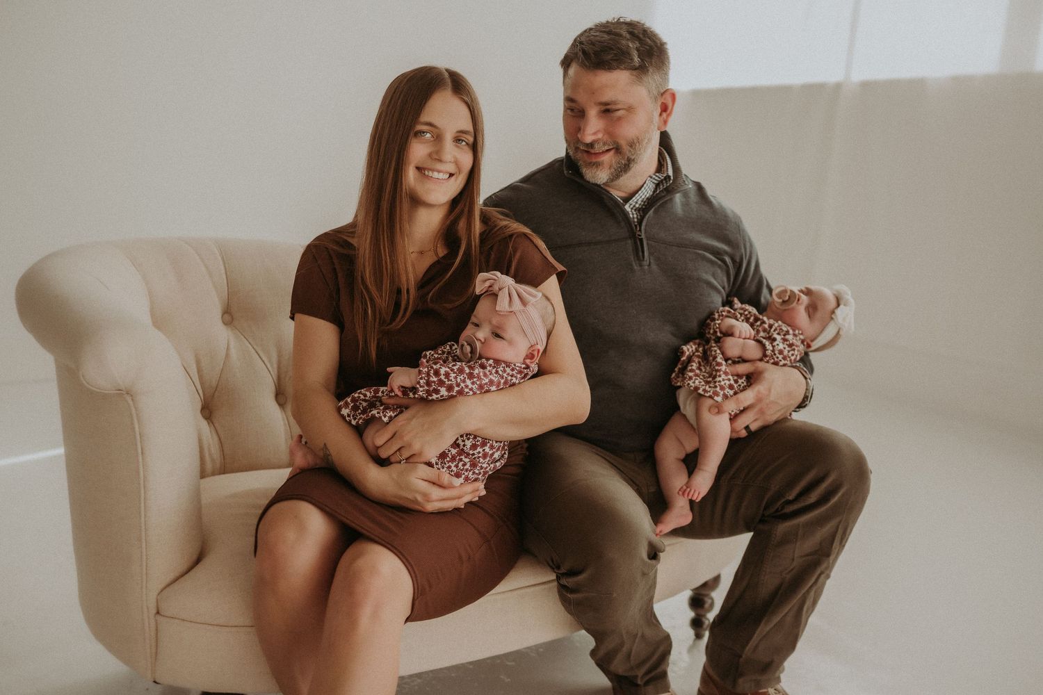 Family portrait featuring twin babies in matching floral outfits on a cream tufted sofa.