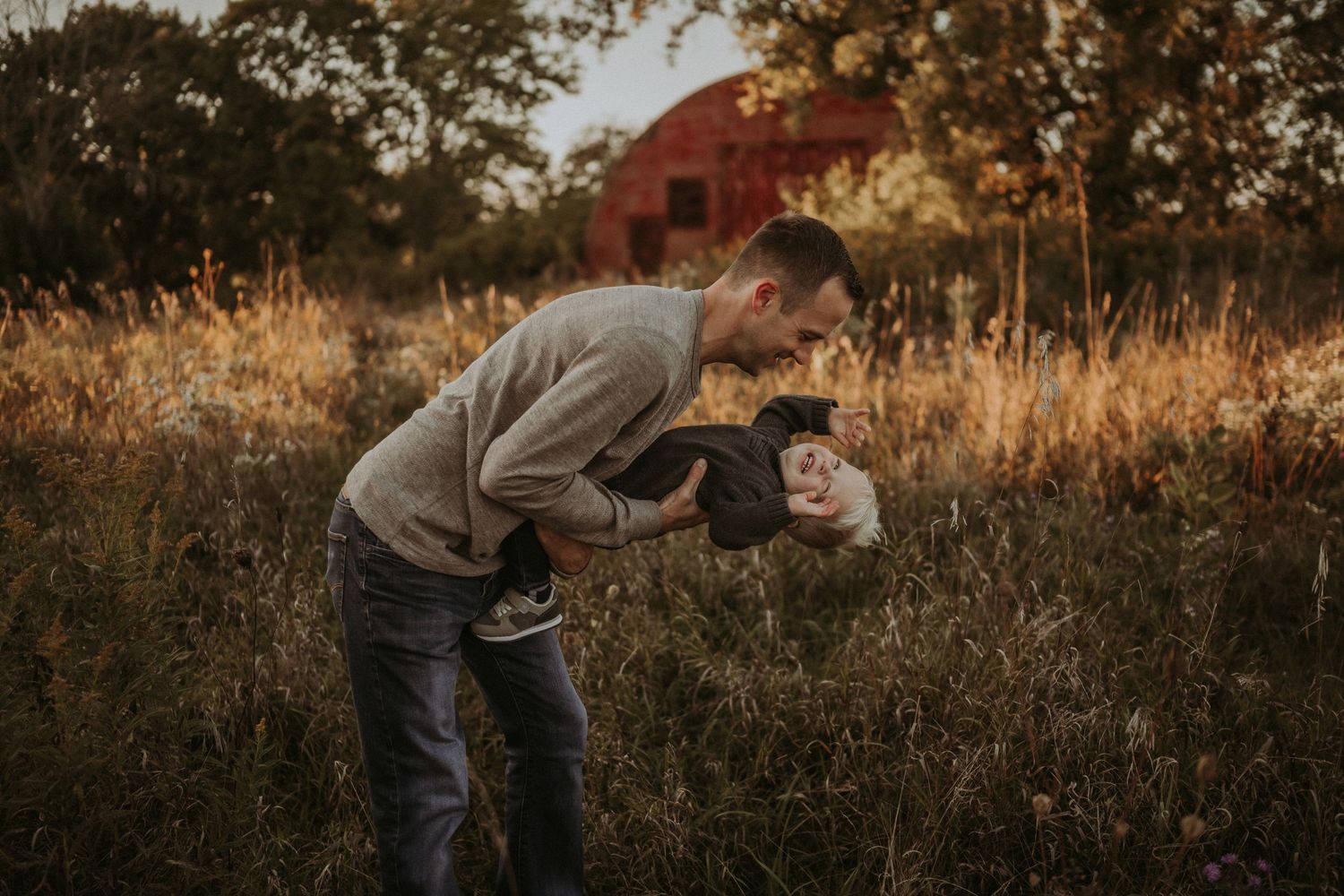 Playful interaction between parent and child in a golden autumn field with red barn backdrop.