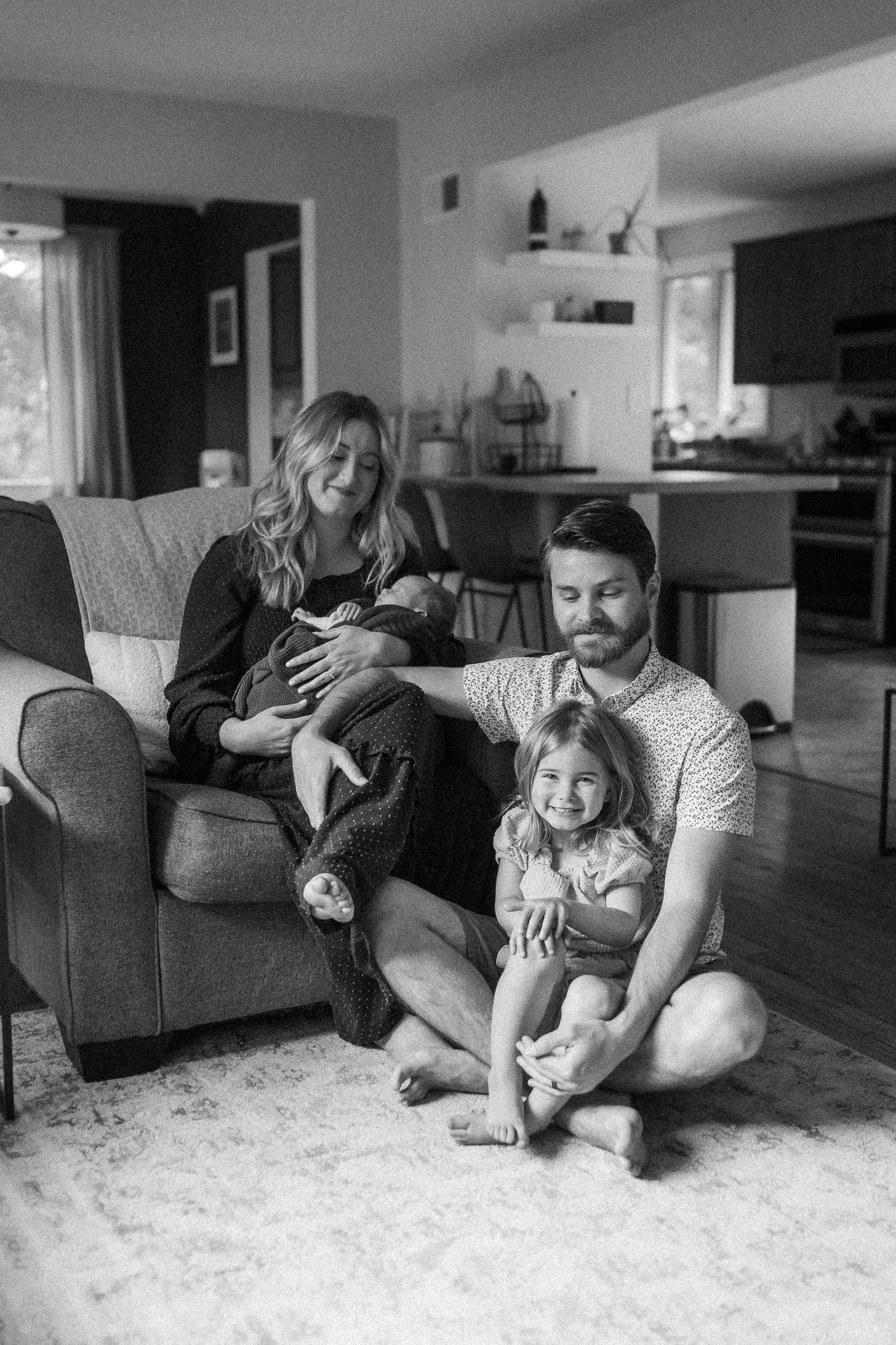 Family lounging together on grey couch in bright, modern living space.