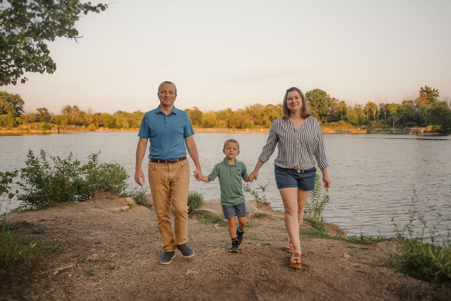 Family silhouetted against sunset sky walking along waterfront path.