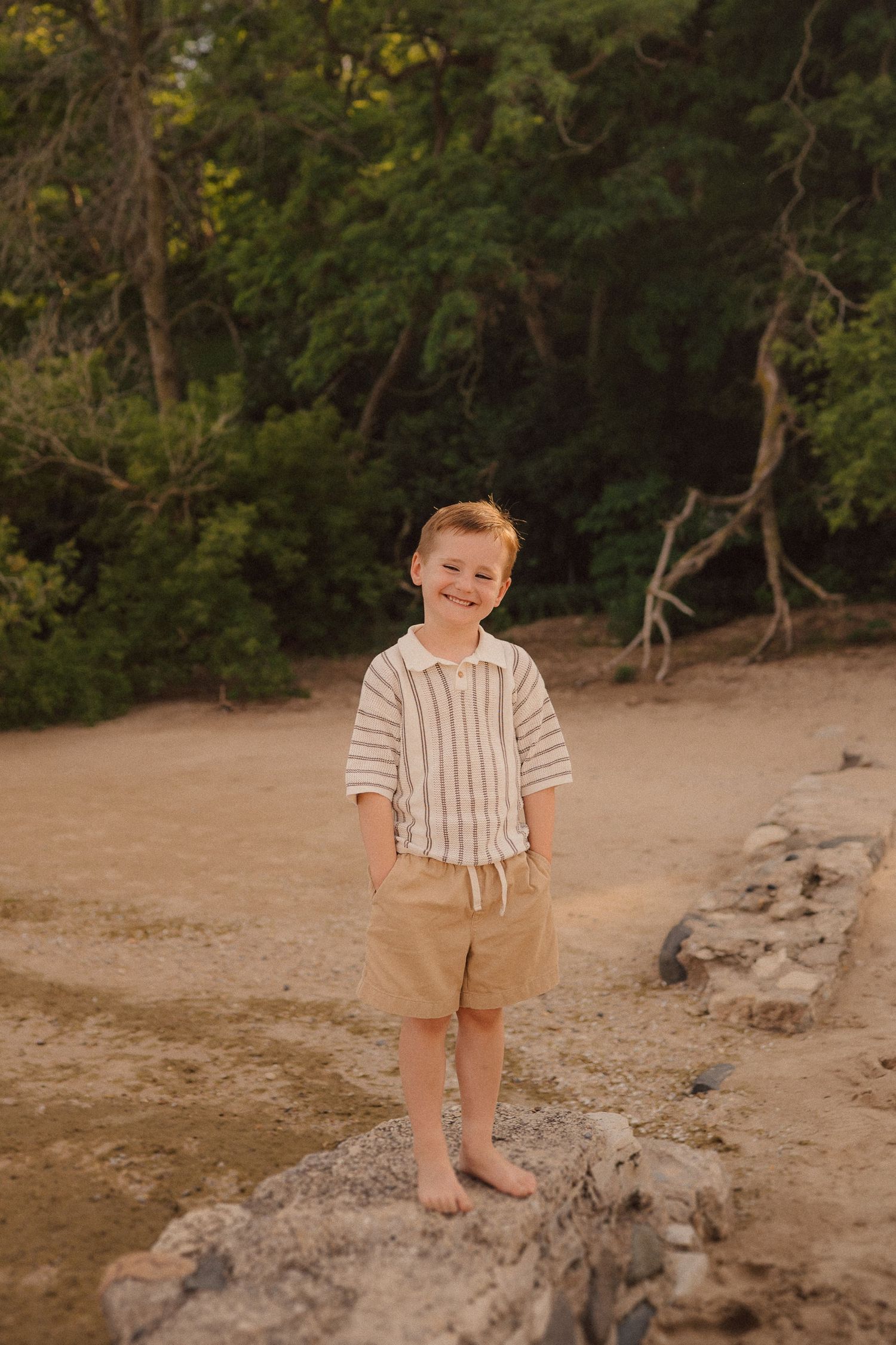 A child plays outdoors on a sandy beach trail surrounded by green trees and natural foliage in warm evening light.