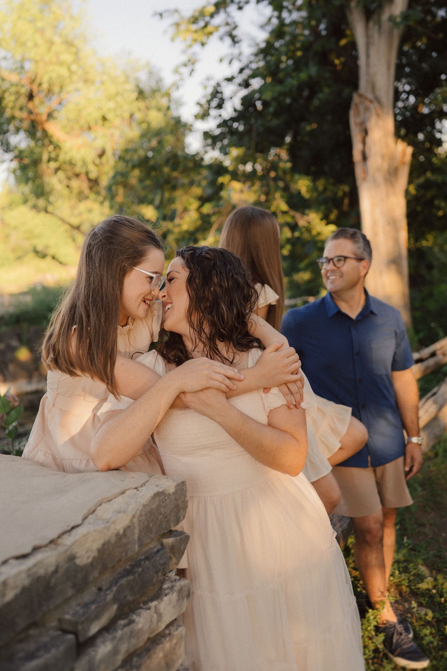 Family members share tender embraces while sitting on rocky outcrop at sunset.