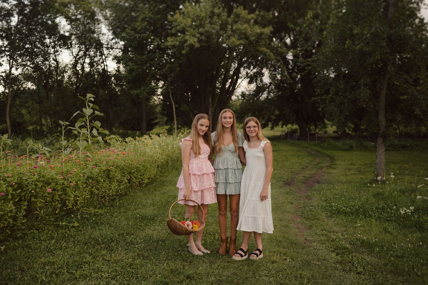 Three people pose together on a rustic dirt path surrounded by lush greenery and trees.