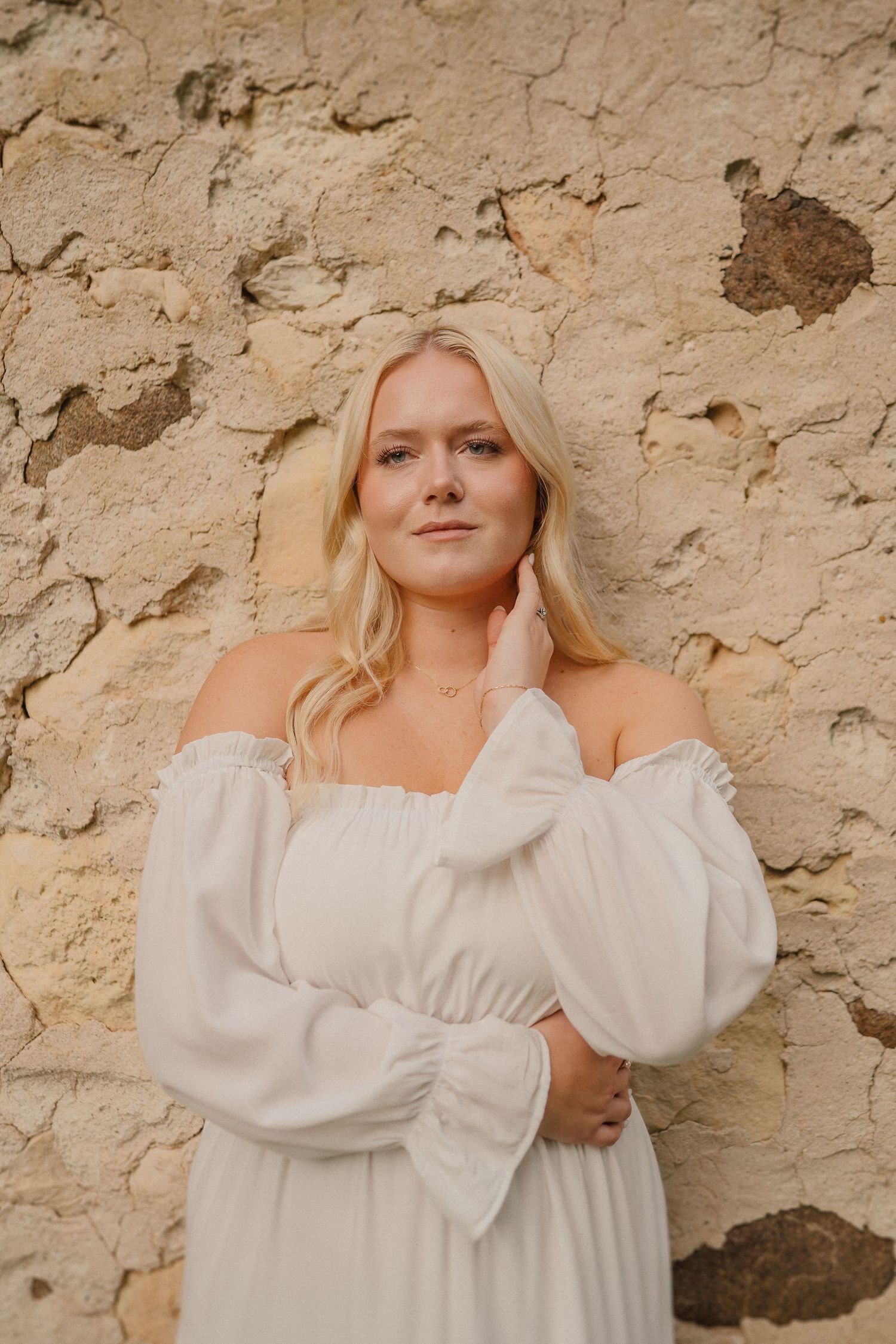A soft and dreamy photoshoot against a textured stone wall featuring an elegant white dress with puff sleeves.