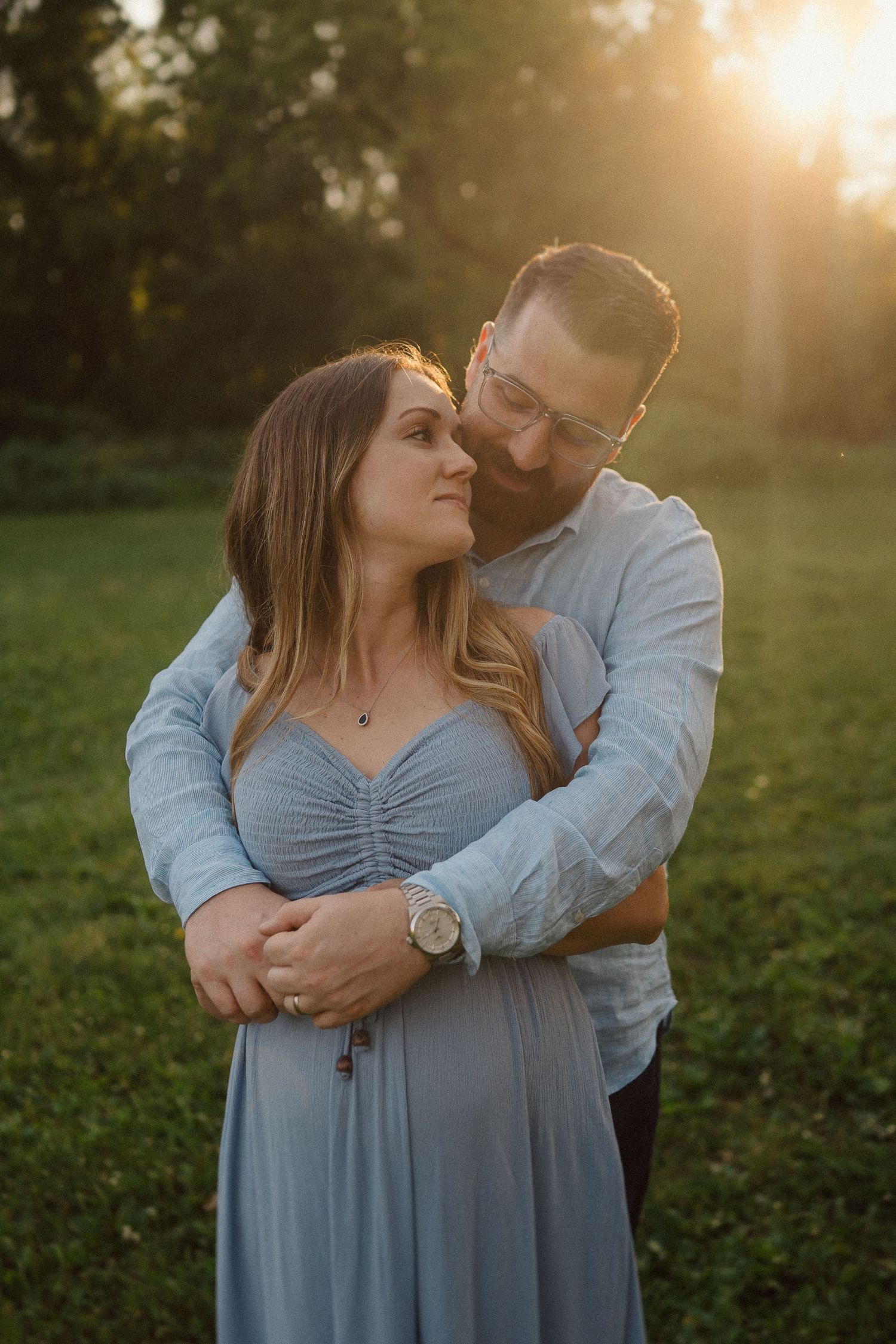 A romantic couple embraces in a sunlit field during golden hour wearing coordinated blue outfits.