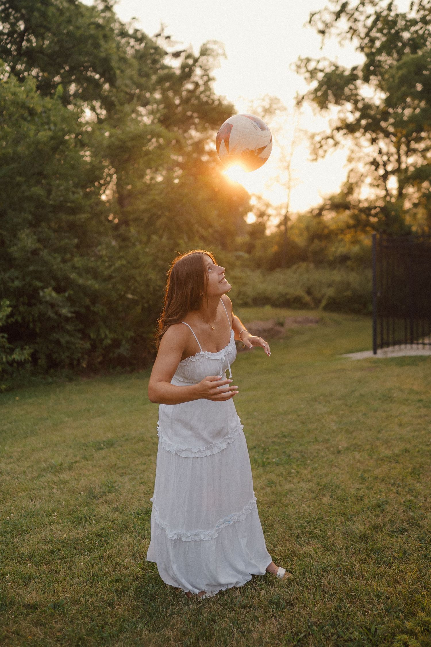 White flowy dress catches golden hour light in a grassy outdoor setting with trees.