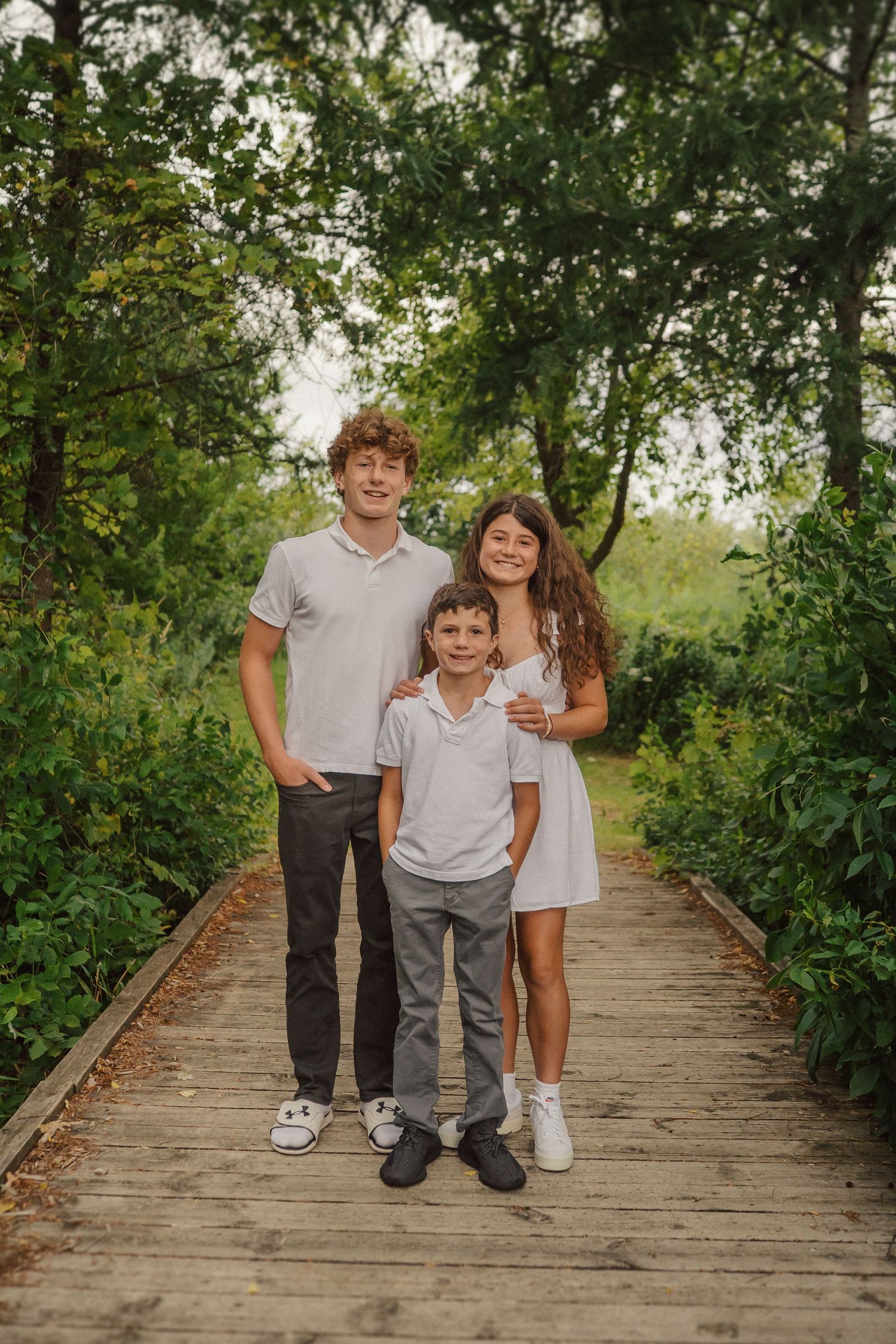 A family photo session on a wooden walkway with green trees and bushes in the background.