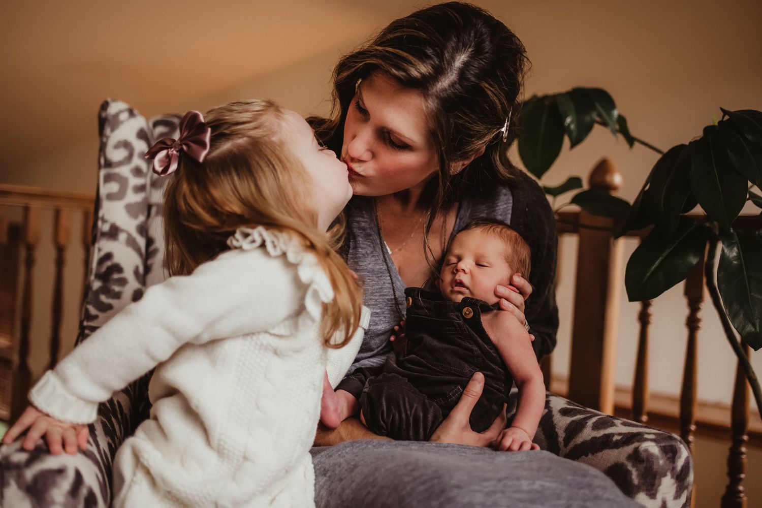 A touching family moment captured on a patterned chair with a houseplant in the background.
