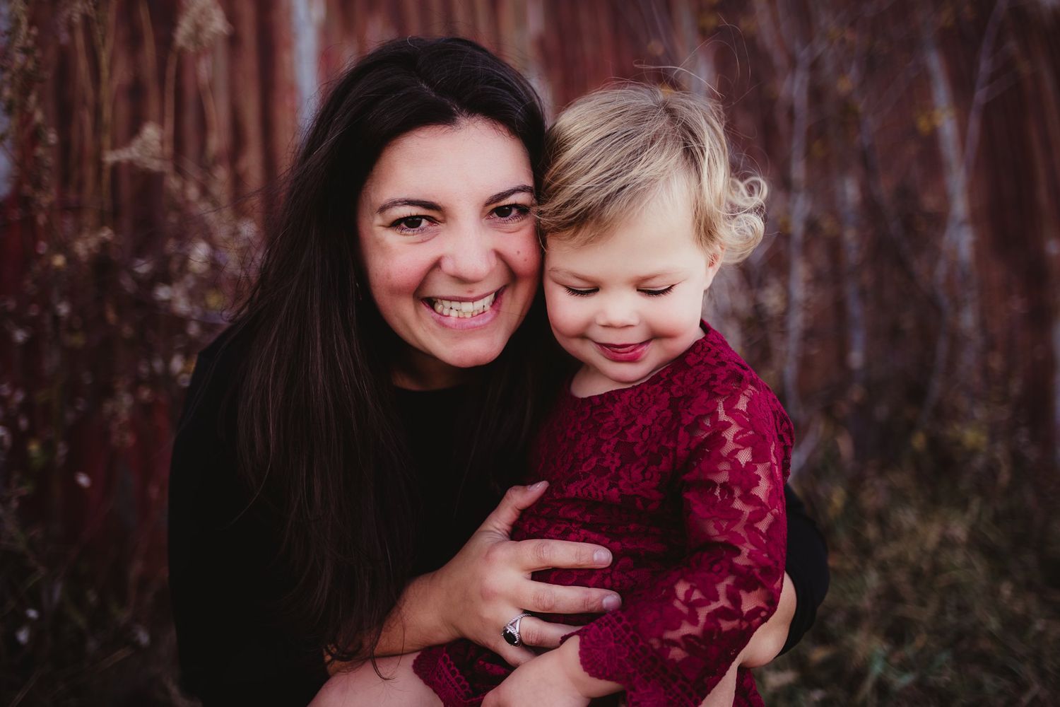 A joyful moment captured between two people wearing black and burgundy against a rustic background.