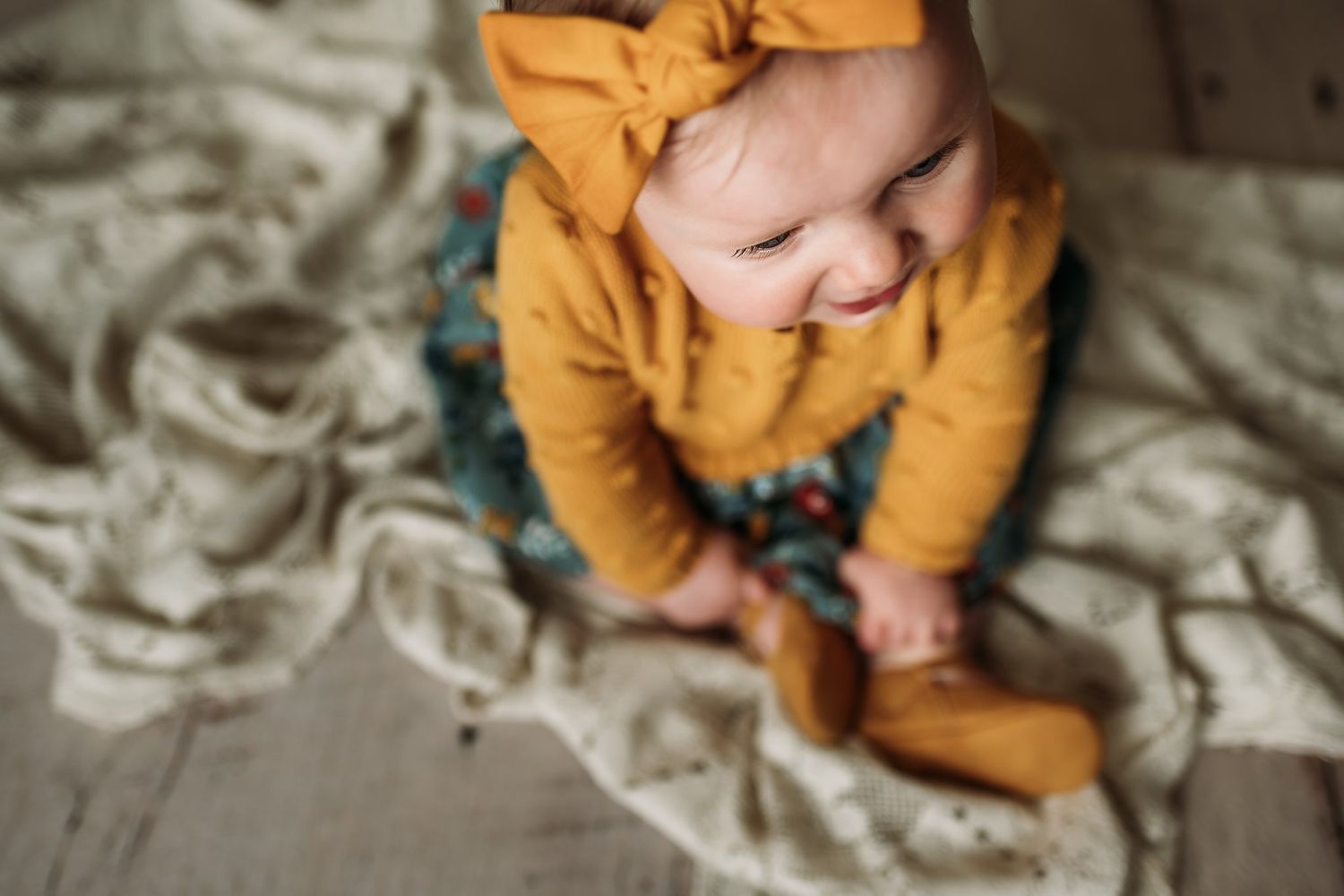 Baby wearing mustard yellow outfit lying on textured fabric in soft lighting.