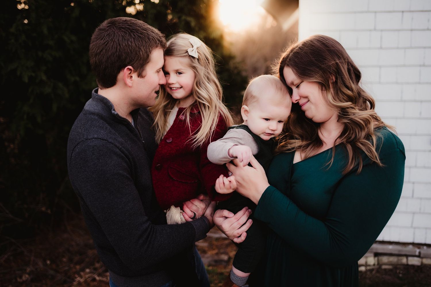 Candid family portrait against white house exterior during golden hour lighting.