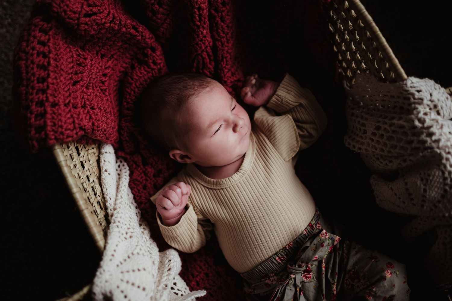 Baby in cream sweater lying on cozy knitted blankets in deep burgundy and white.