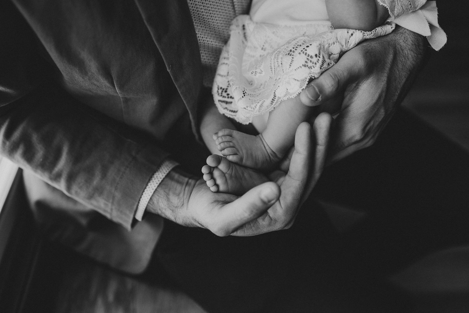 Black and white detail shot of hands gently cradling a newborn in lace.