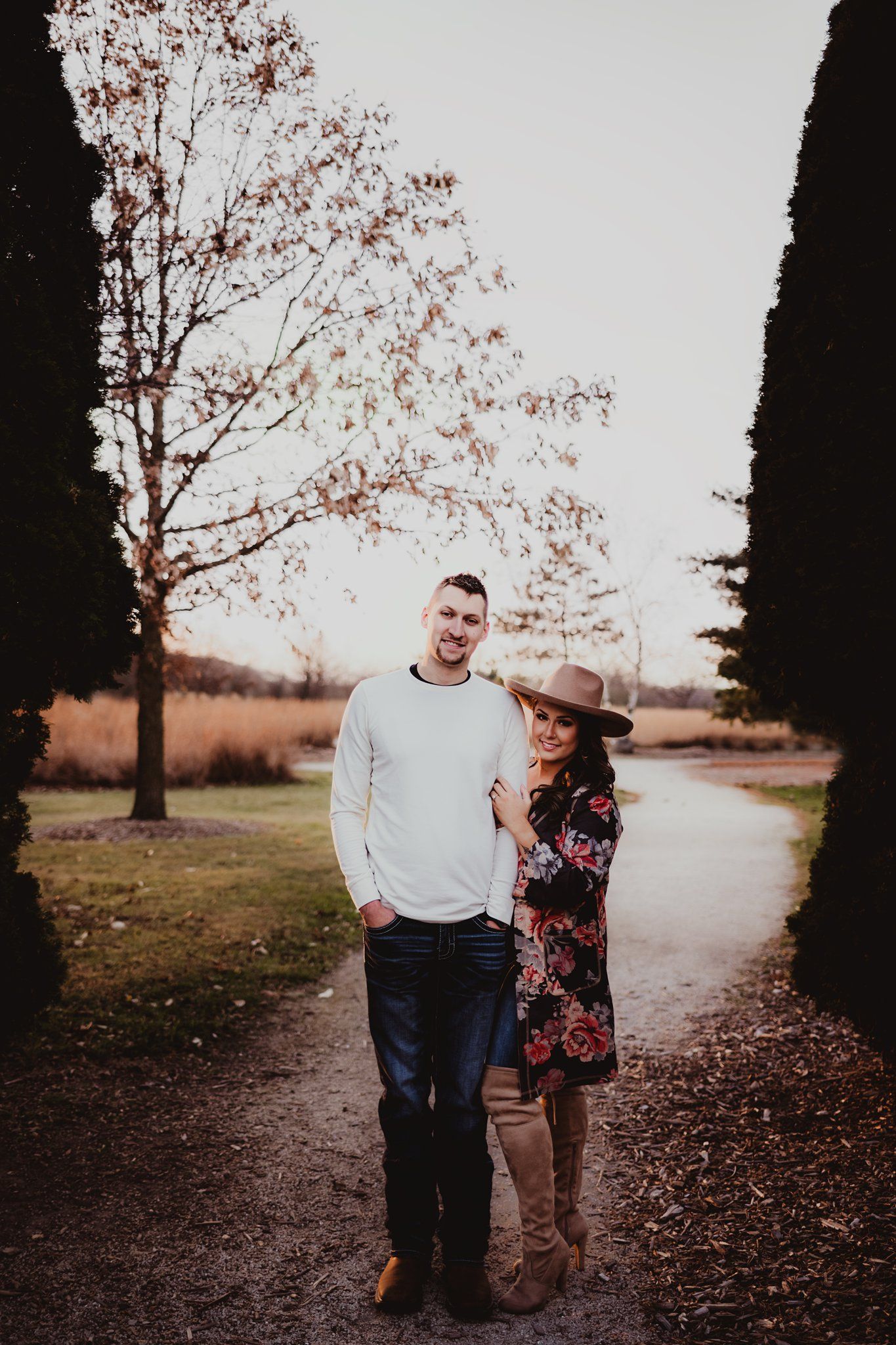 Autumn pathway portrait with tall cypress trees framing couple in casual attire.