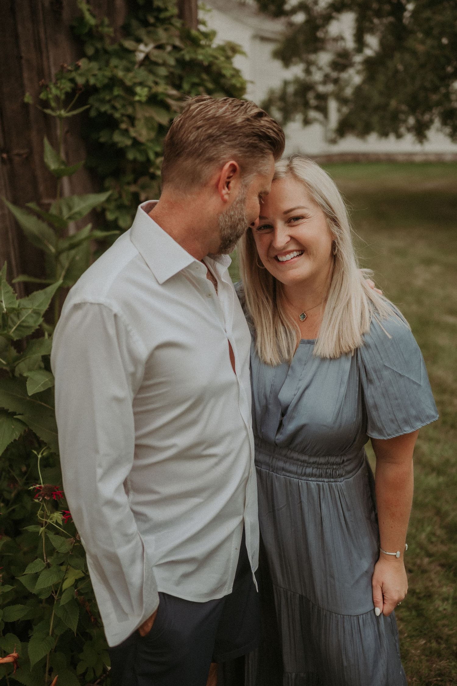 Intimate portrait of a couple sharing a tender moment in front of a rustic barn wall.