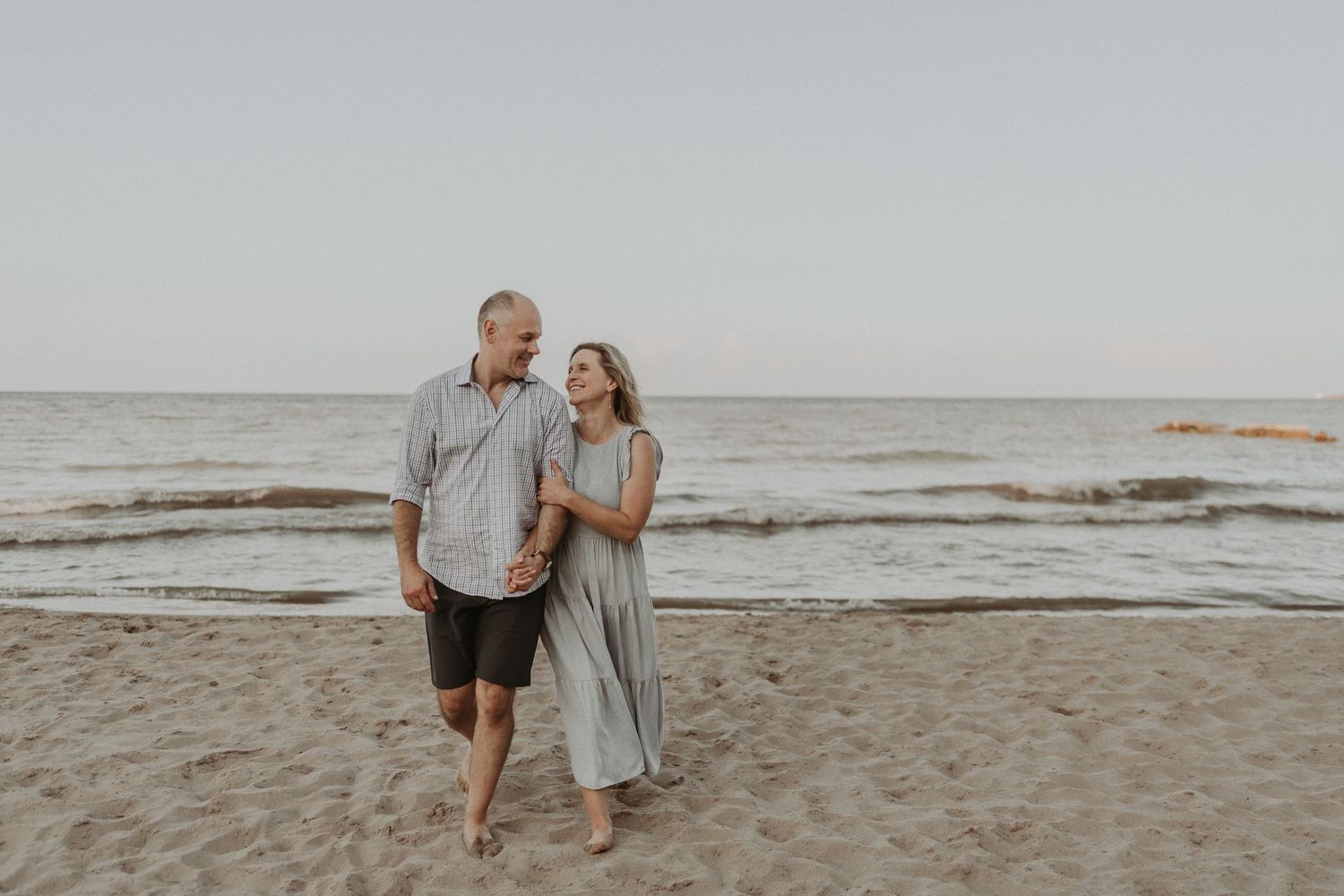 Couple walking together on sandy beach during golden hour.