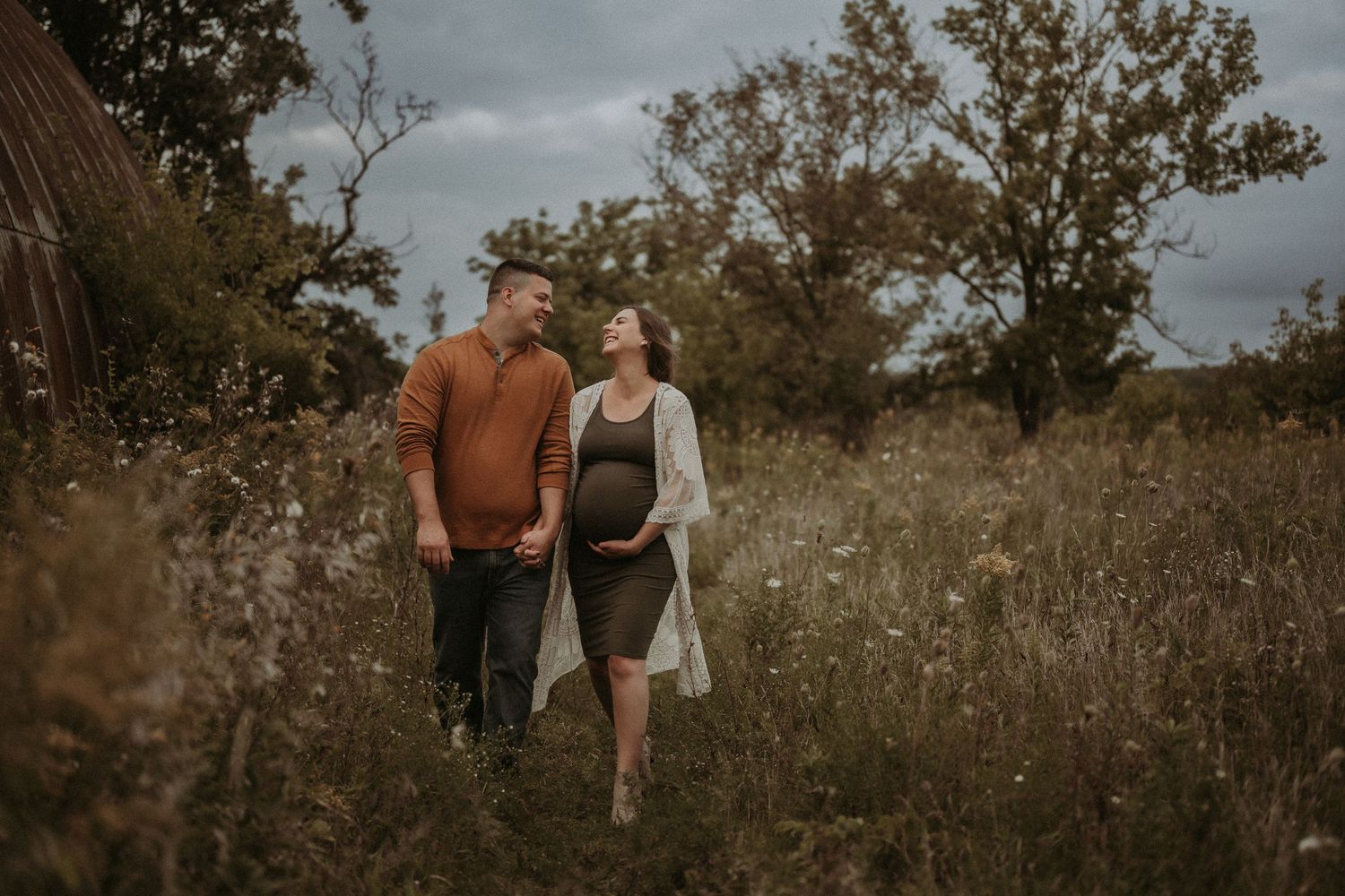 A couple takes a stroll through a wildflower field during their maternity photoshoot.