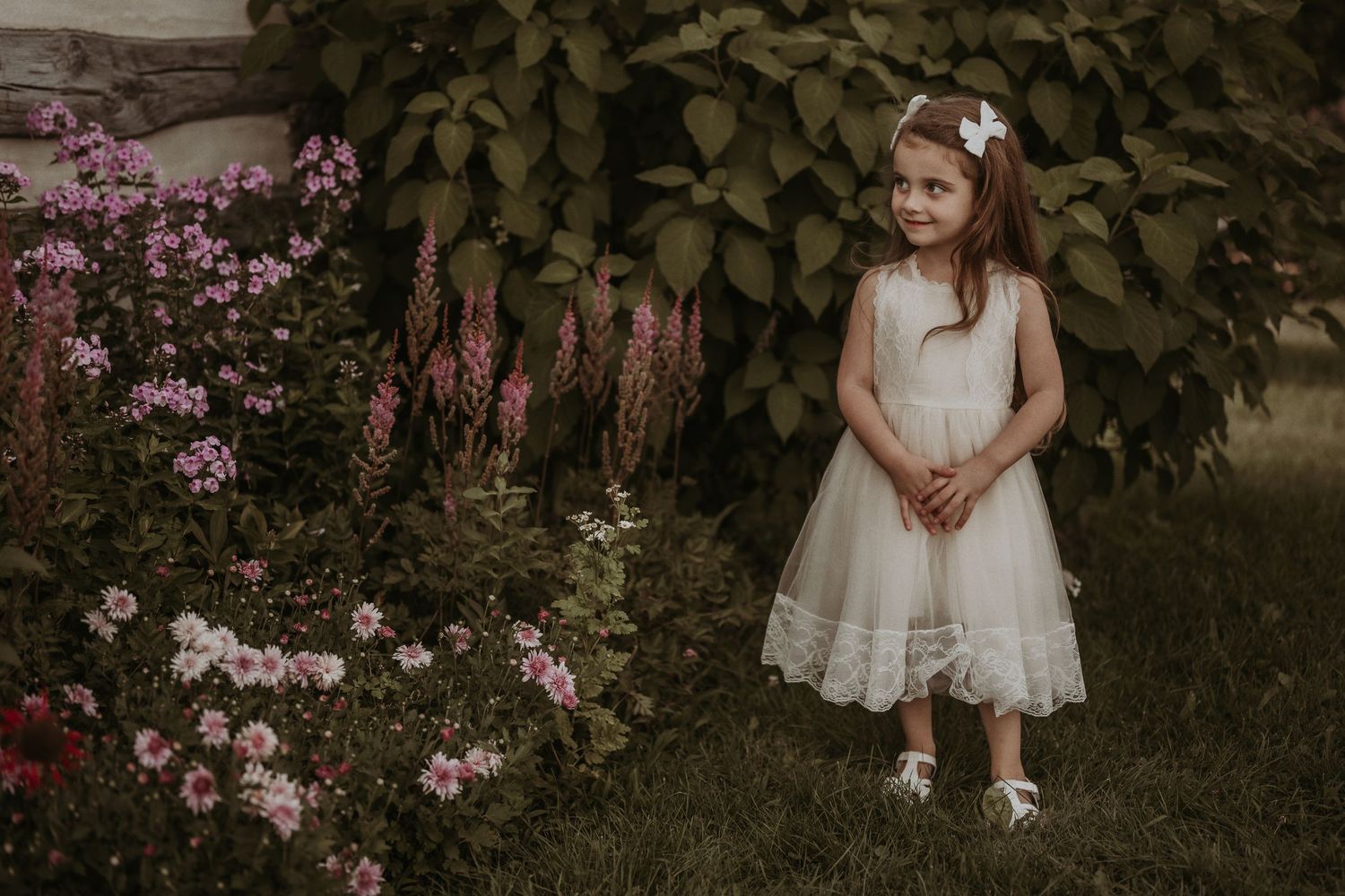 White lace dress photographed in garden setting with pink flowers and greenery.