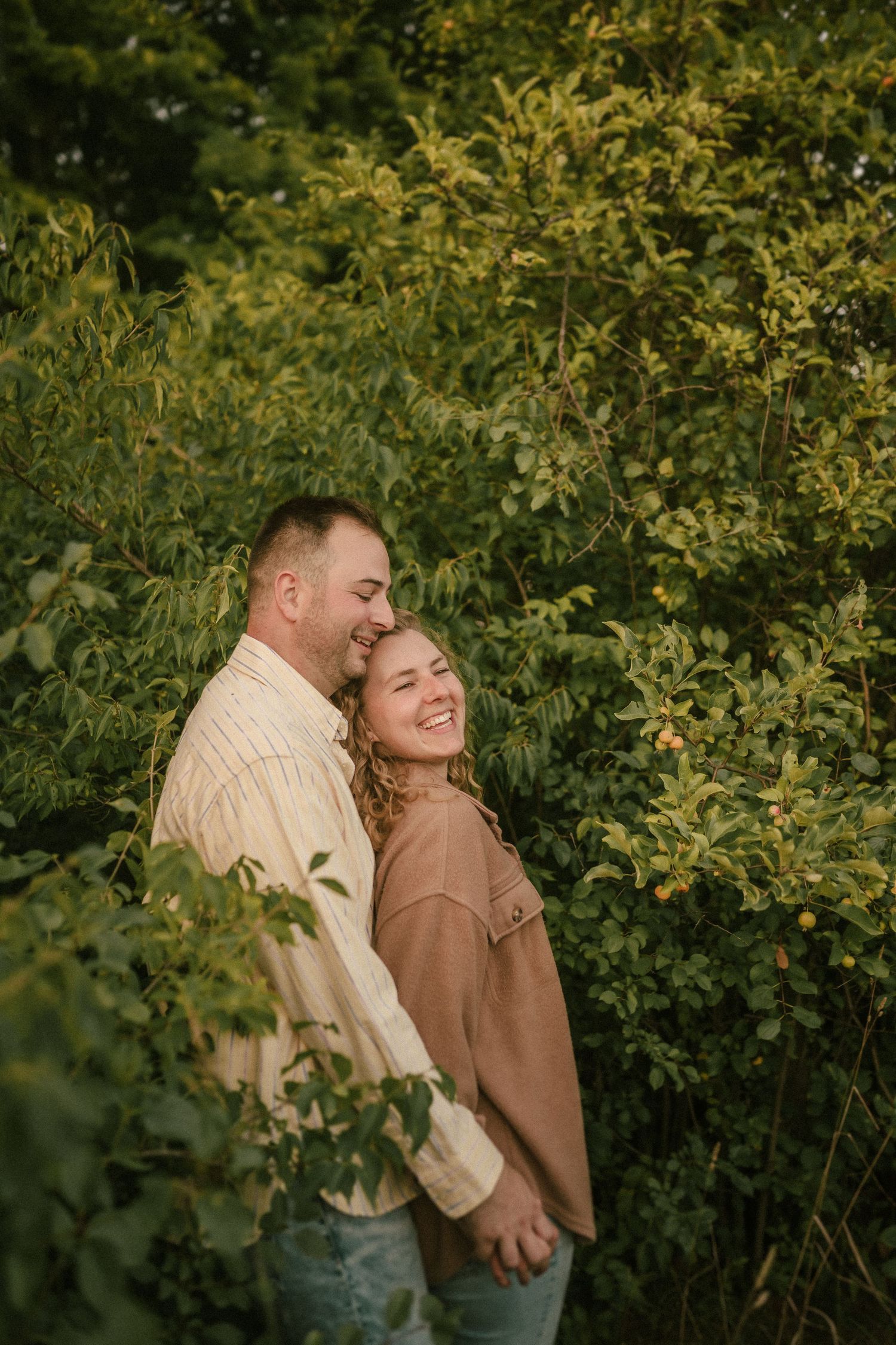 Couple shares tender moment among green foliage during sunset photoshoot.