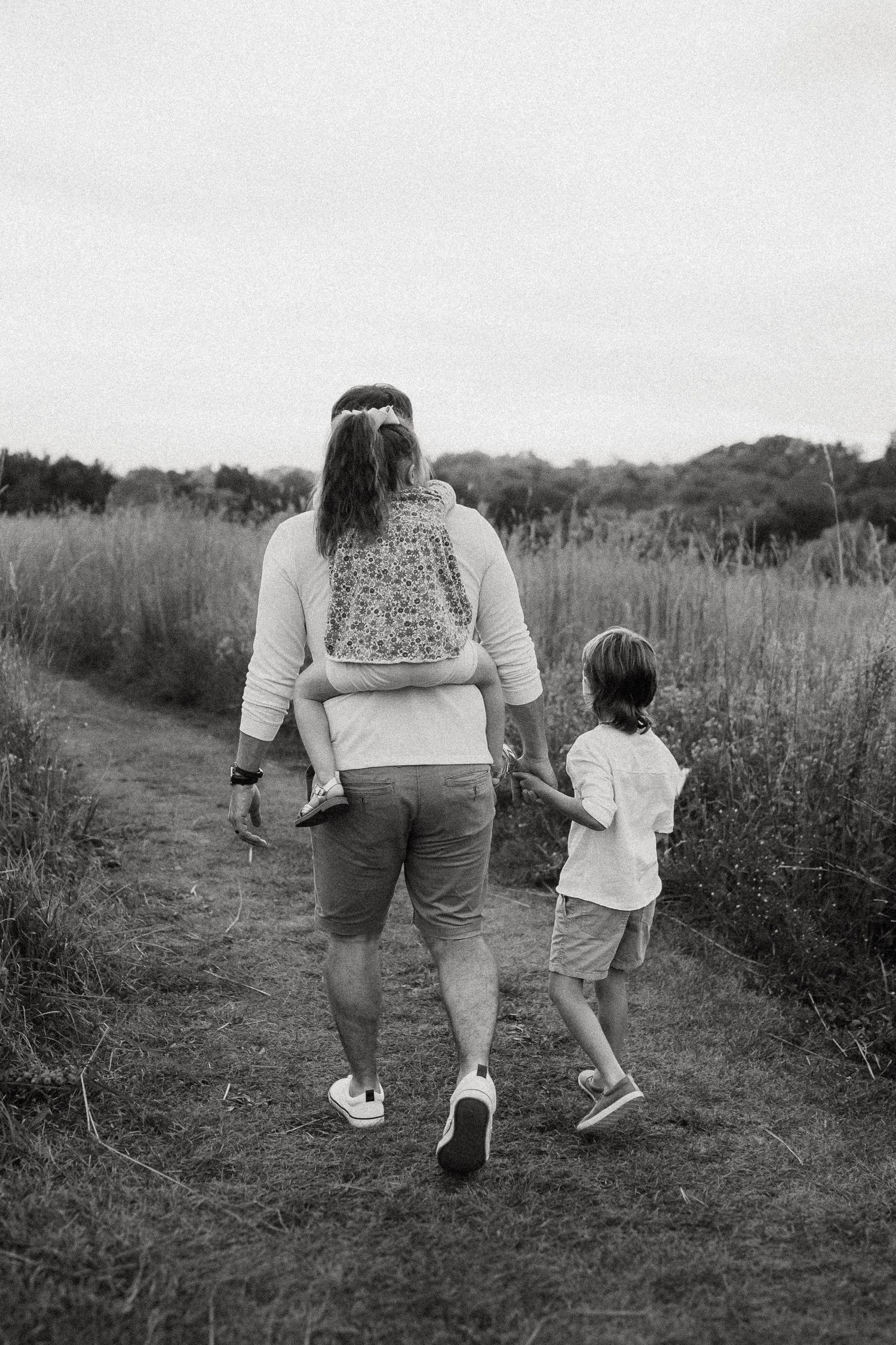 Back view of two people walking together on a nature trail surrounded by tall grass.